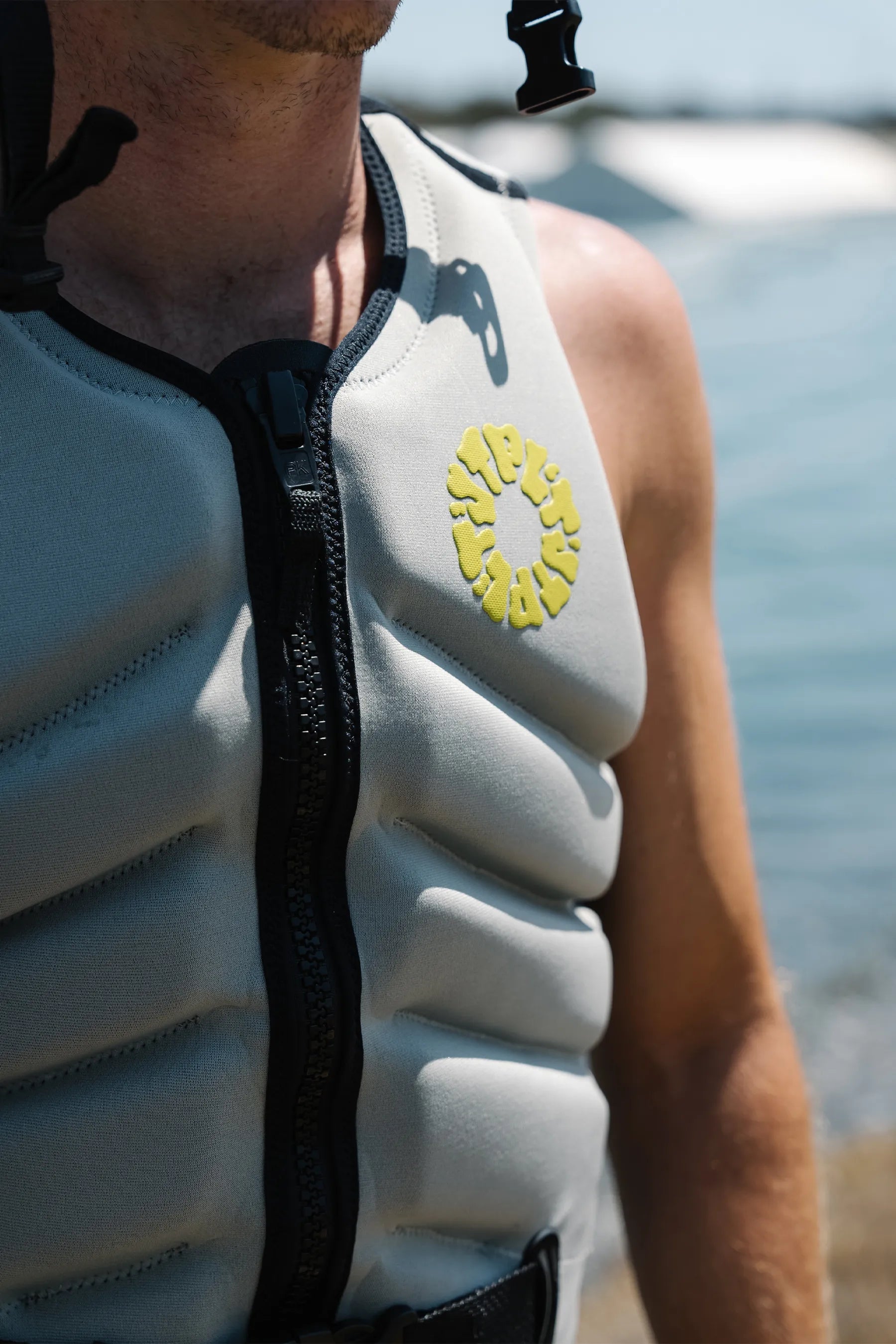 Person wearing a gray life jacket with a yellow logo near water