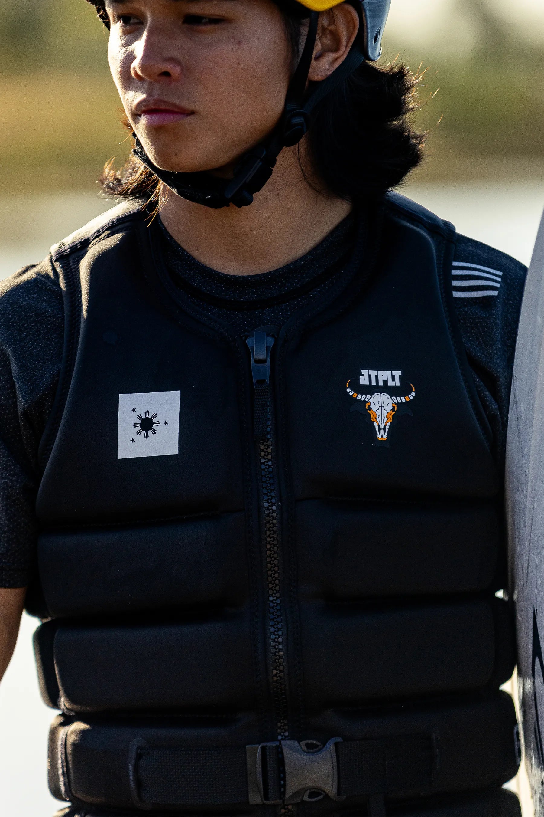 Person wearing a Jetpilot X1 Life Jacket - Raph Trinidad Signature Series - Black with logos, standing outdoors.