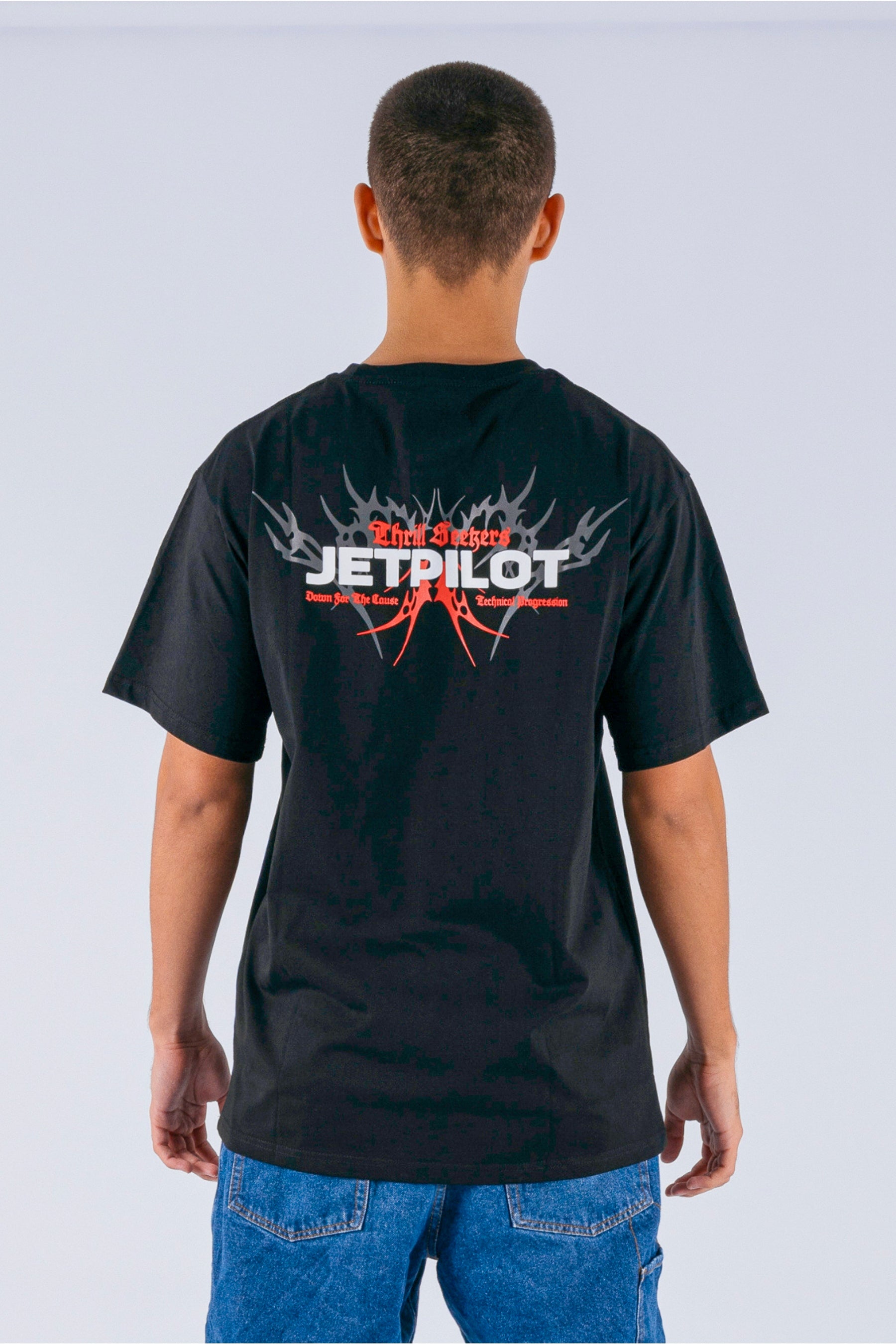Back view of a person wearing a black tee with a white Jetpilot logo on a white background — view 2 (3)
