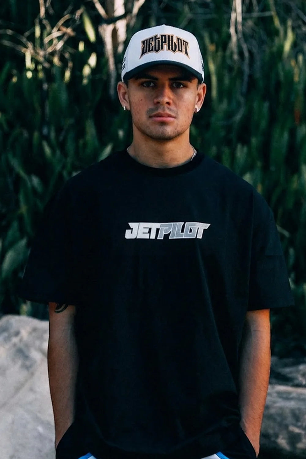 Male in Black t shirt with big two-tone (grey and white) "JETPILOT" logo, against an Australian backyard garden and forest.