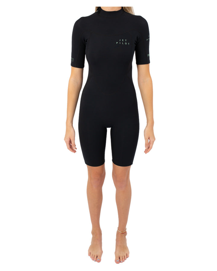 A woman standing straight facing forward wearing a black Jetpilot Flight 2X2 Womens Springsuit with short sleeves and short l