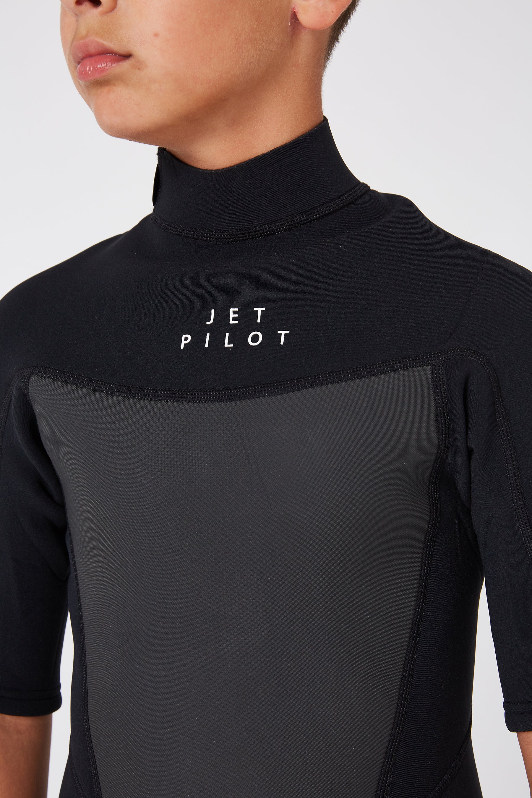 A close-up image of a child wearing the Jetpilot Flight Youth 2/2Mm Short Sleeve Springsuit in black, showcasing the chest an