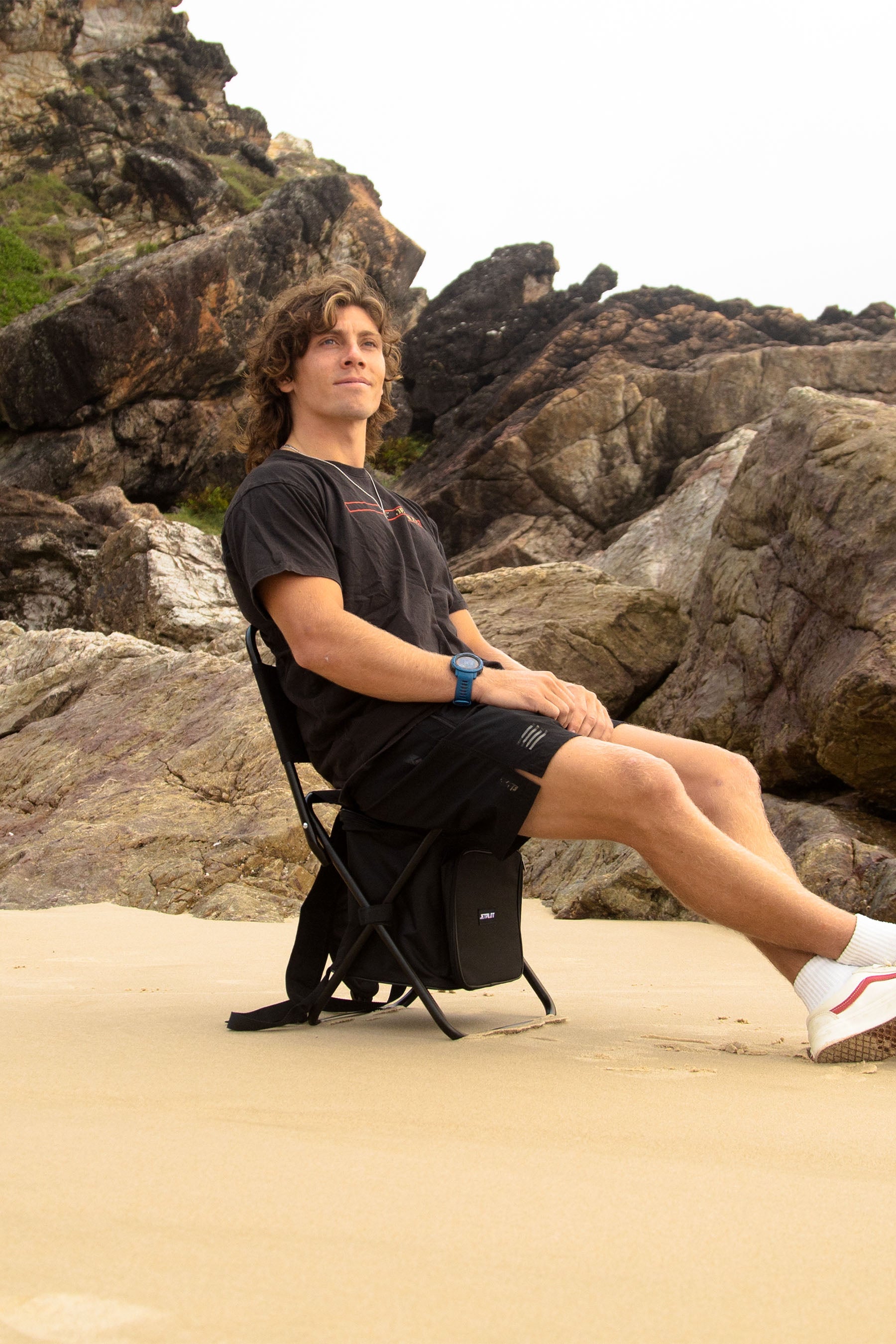 Person sitting on a folding Jetpilot Back Rest Chilled Seat Bag - Black on a rocky beach — image 2