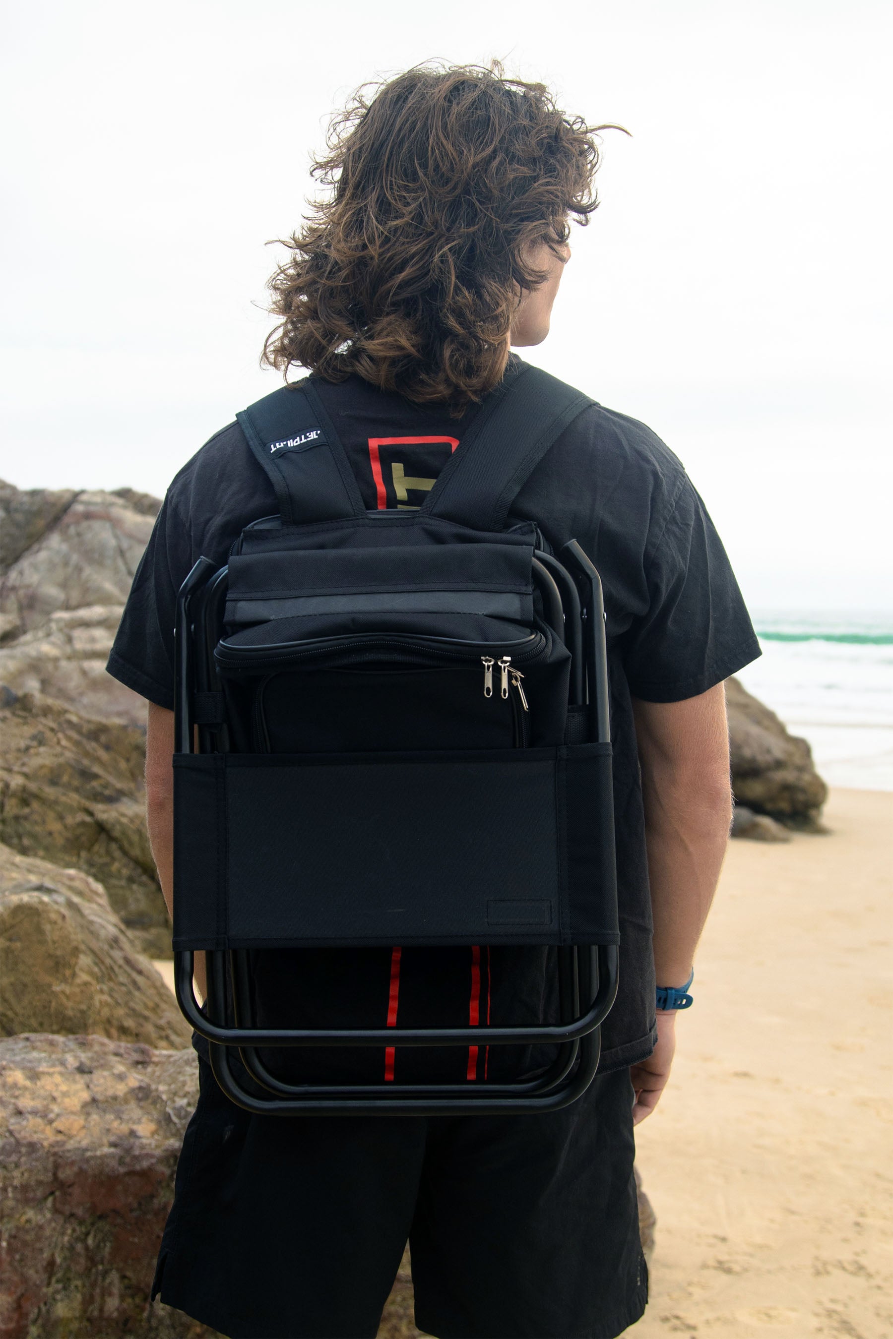 Person wearing a Jetpilot Back Rest Chilled Seat Bag - Black in backpack mode with a unique design on a beach — image 2