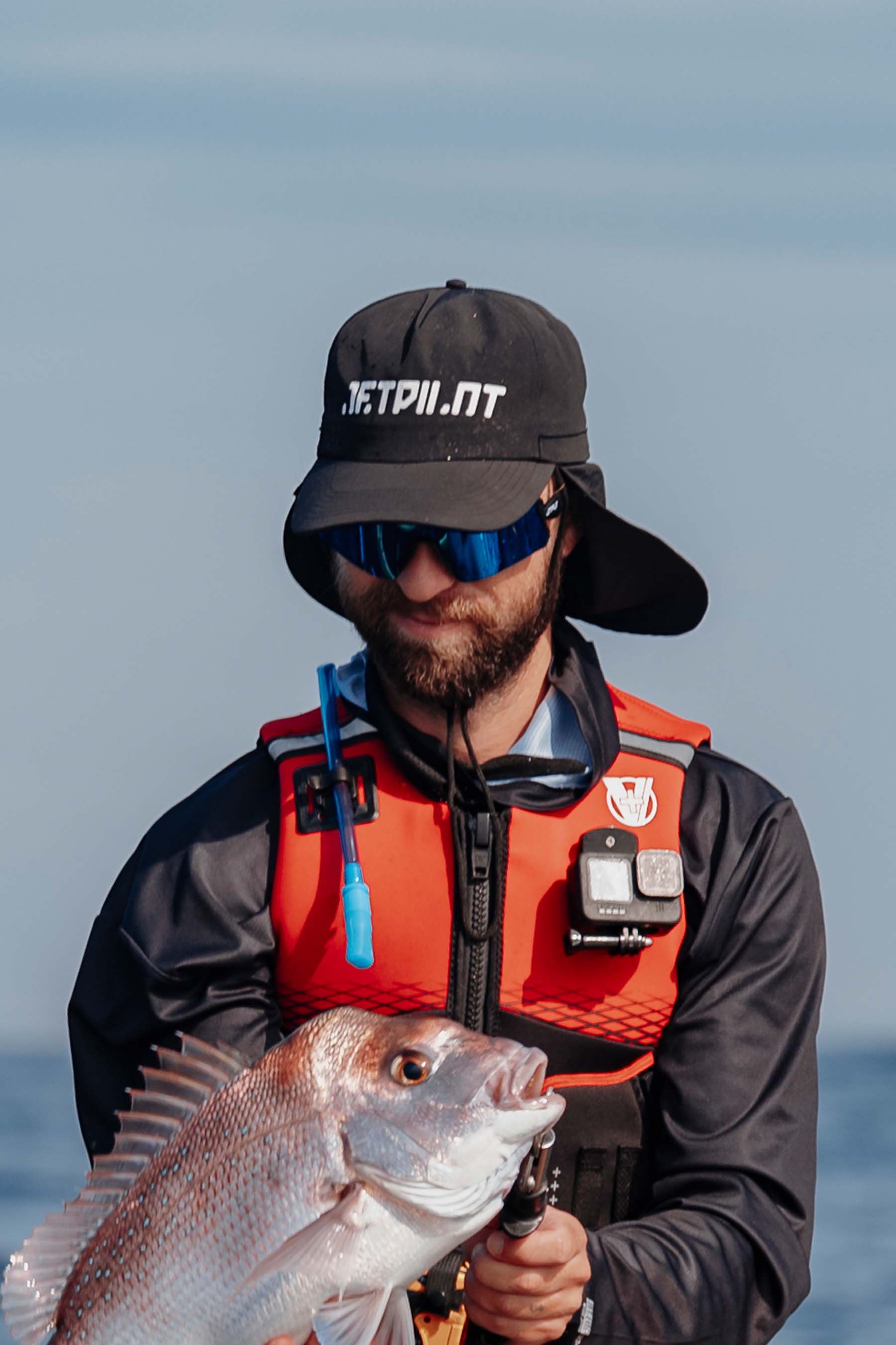 Man holding a fish with a Jetpilot Venture Legionaire Mens Cap - Black and life jacket on a clear day