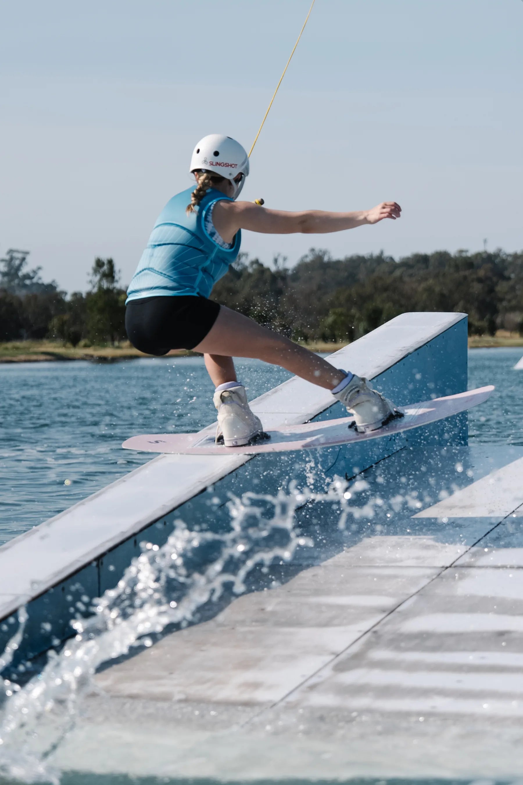 Person wakeboarding on a rail over water with trees in the background — image 2