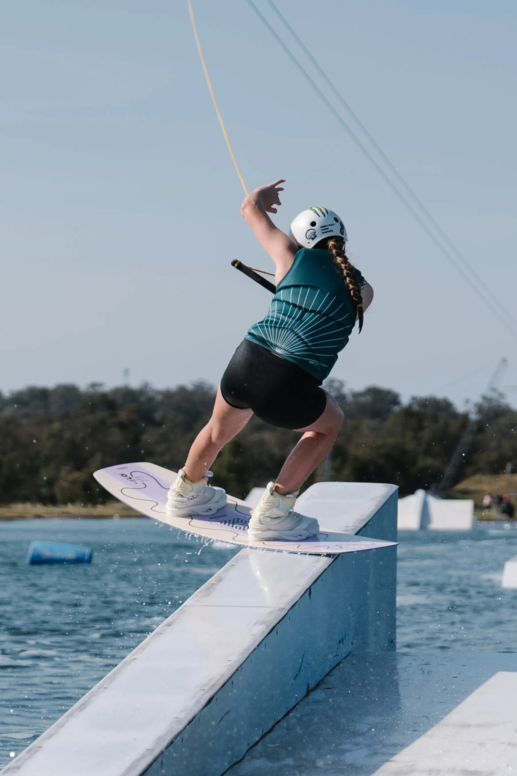Person wakeboarding on a rail with a clear sky and water background, wearing the Jetpilot Allure Ladies Life Jacket - Green