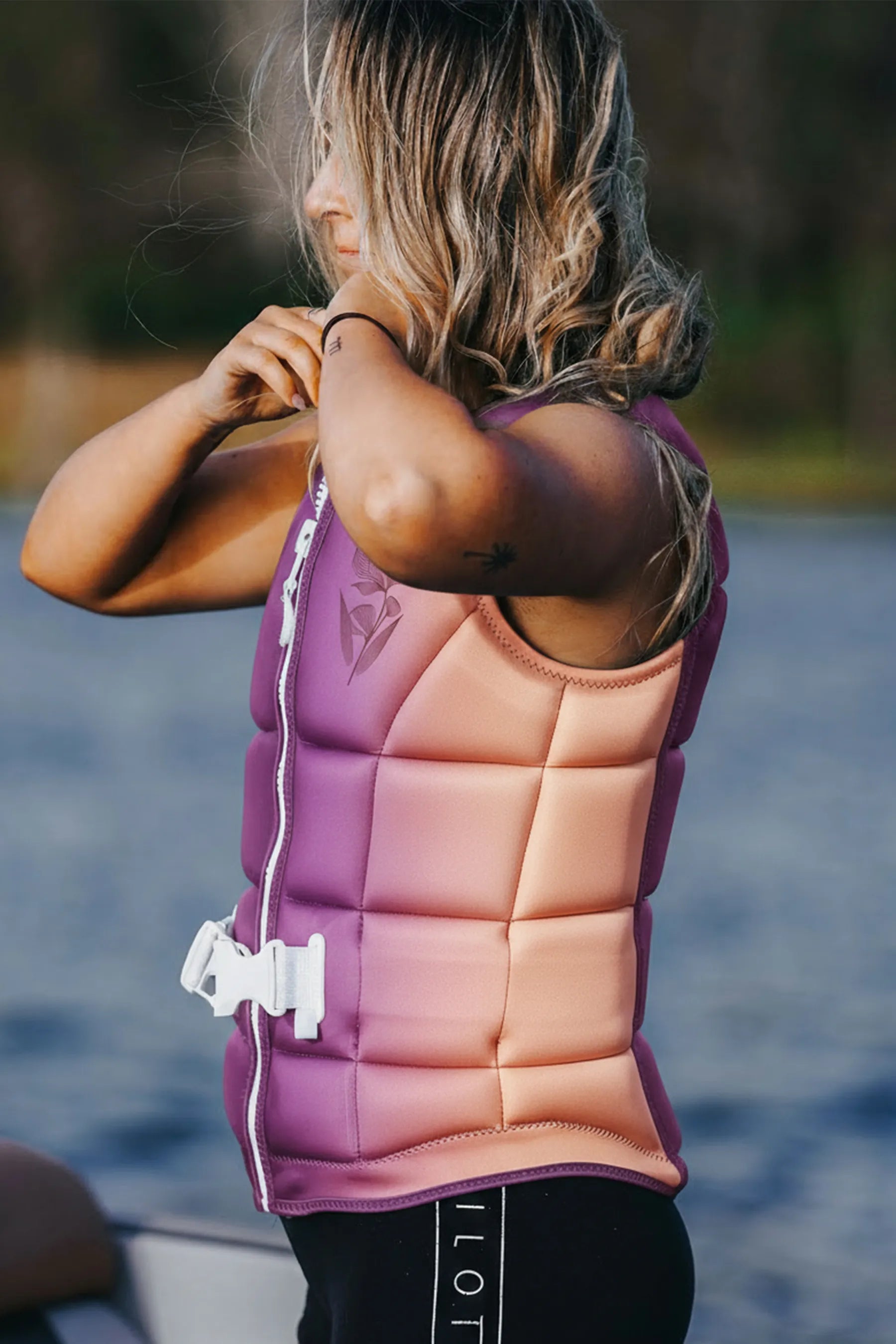 Person wearing a pink and purple life jacket by a body of water
