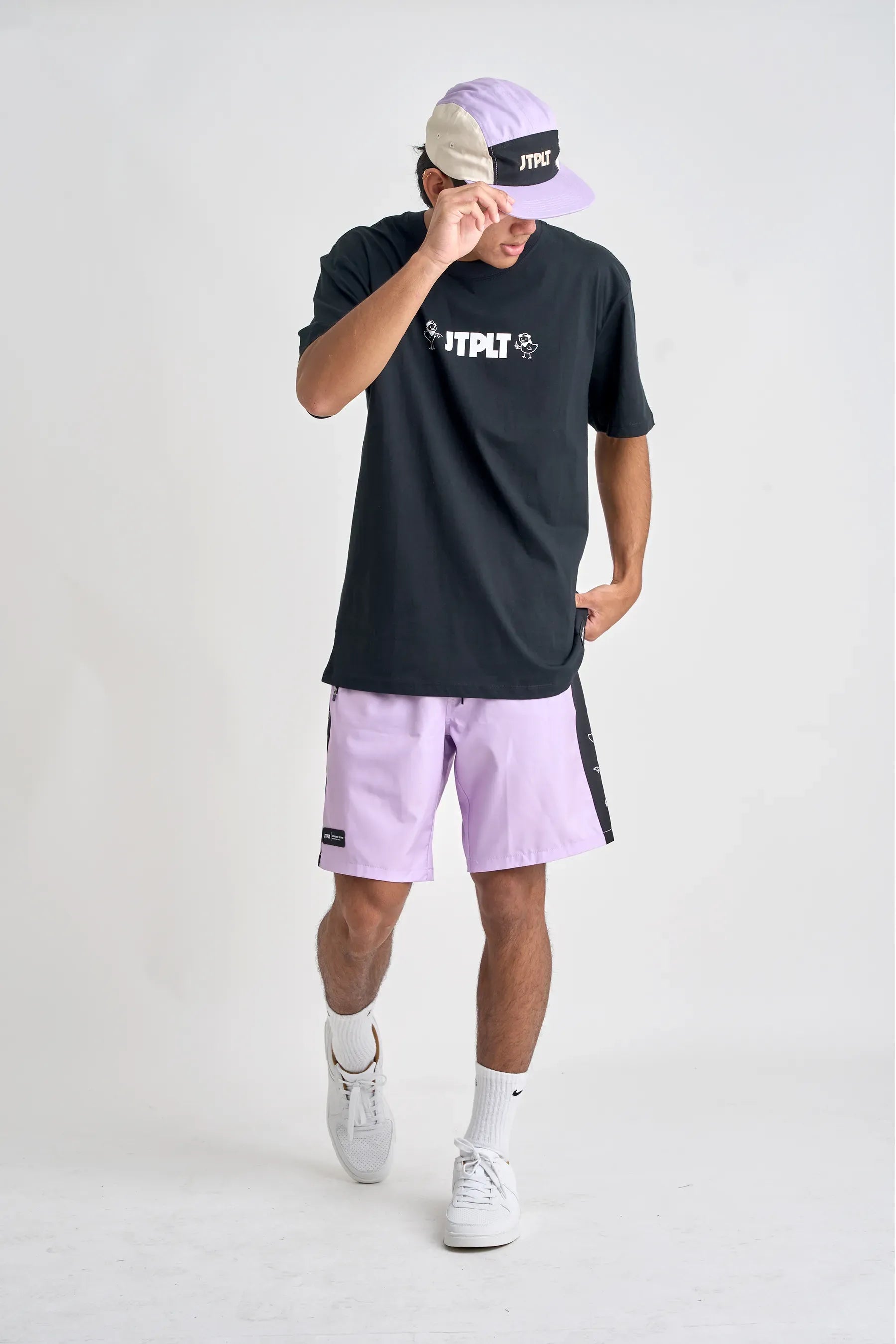 Person wearing a black t-shirt, light purple shorts, and a cap with visible branding on a white background