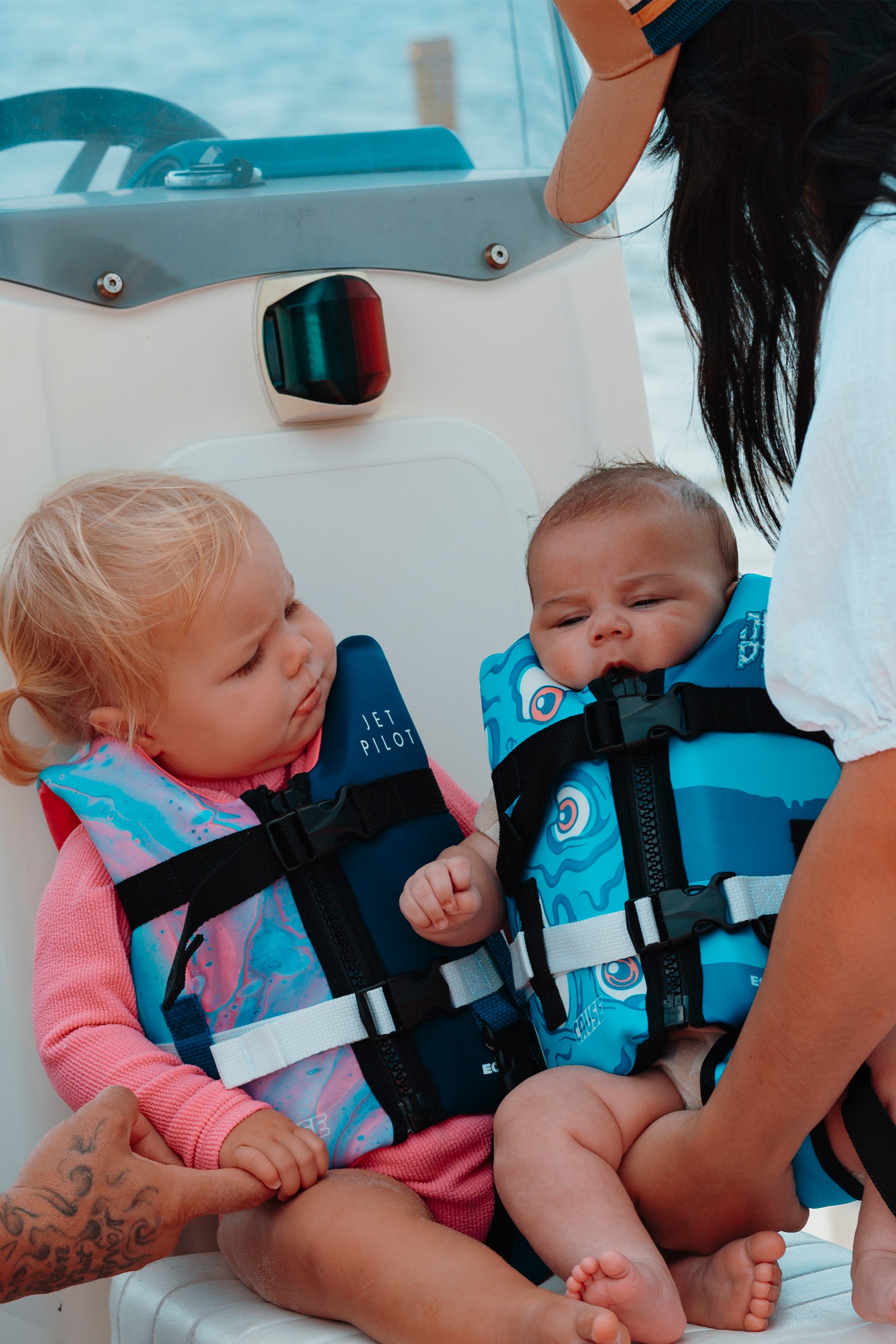 Two children in life vests on a boat with an adult beside them.