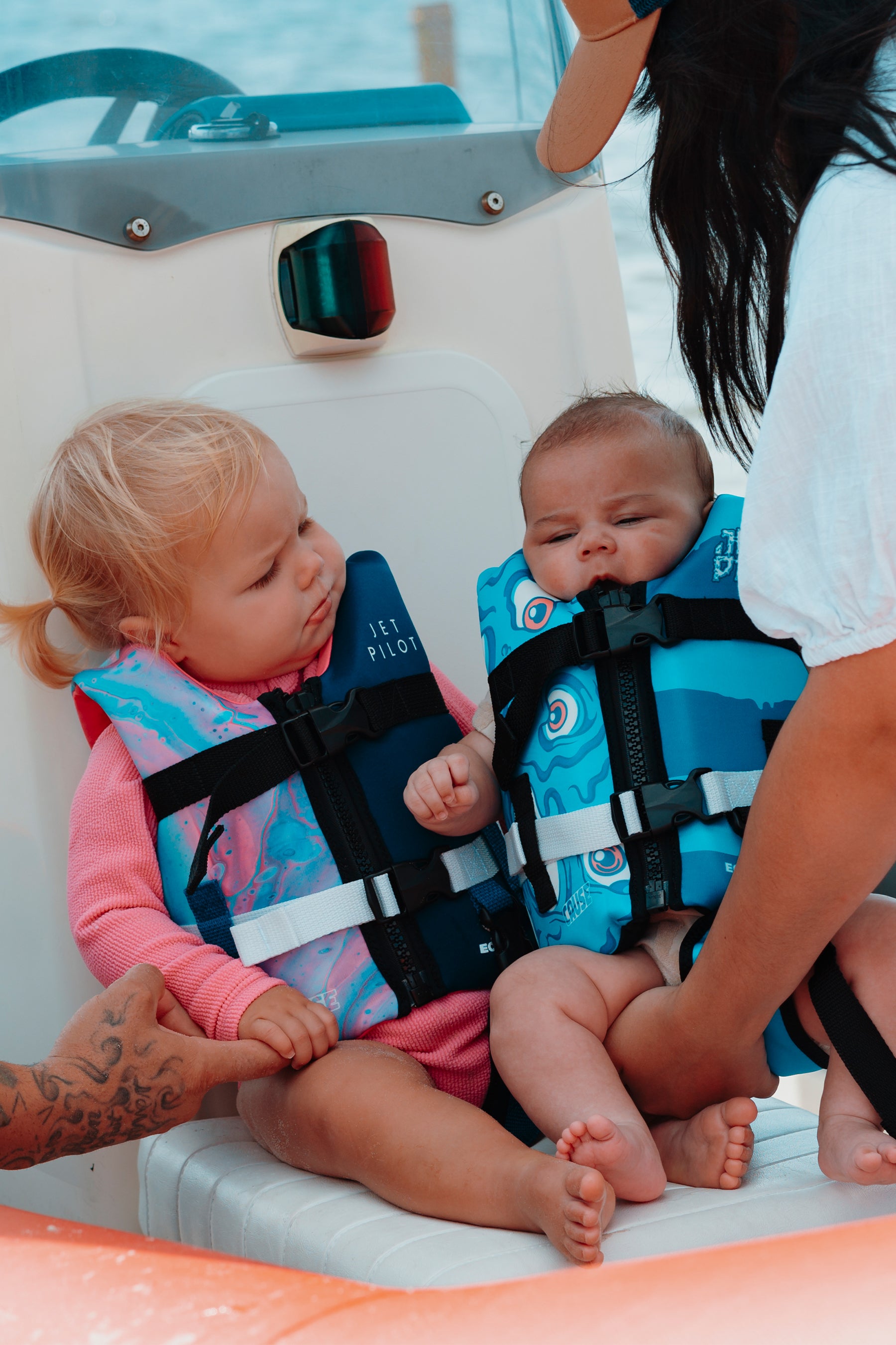 Two children wearing life jackets on a boat with an adult assisting.