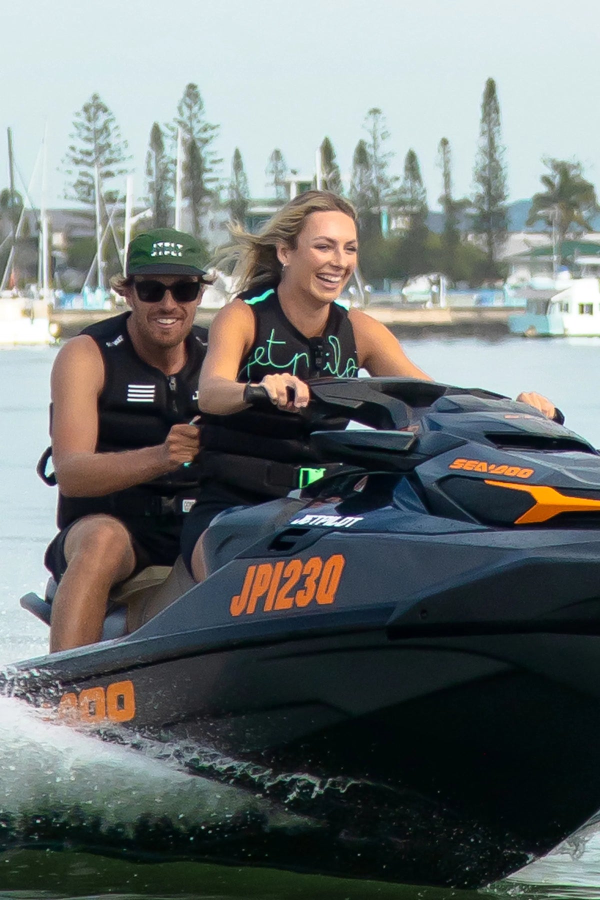 Two people riding a jet ski on water with trees and buildings in the background