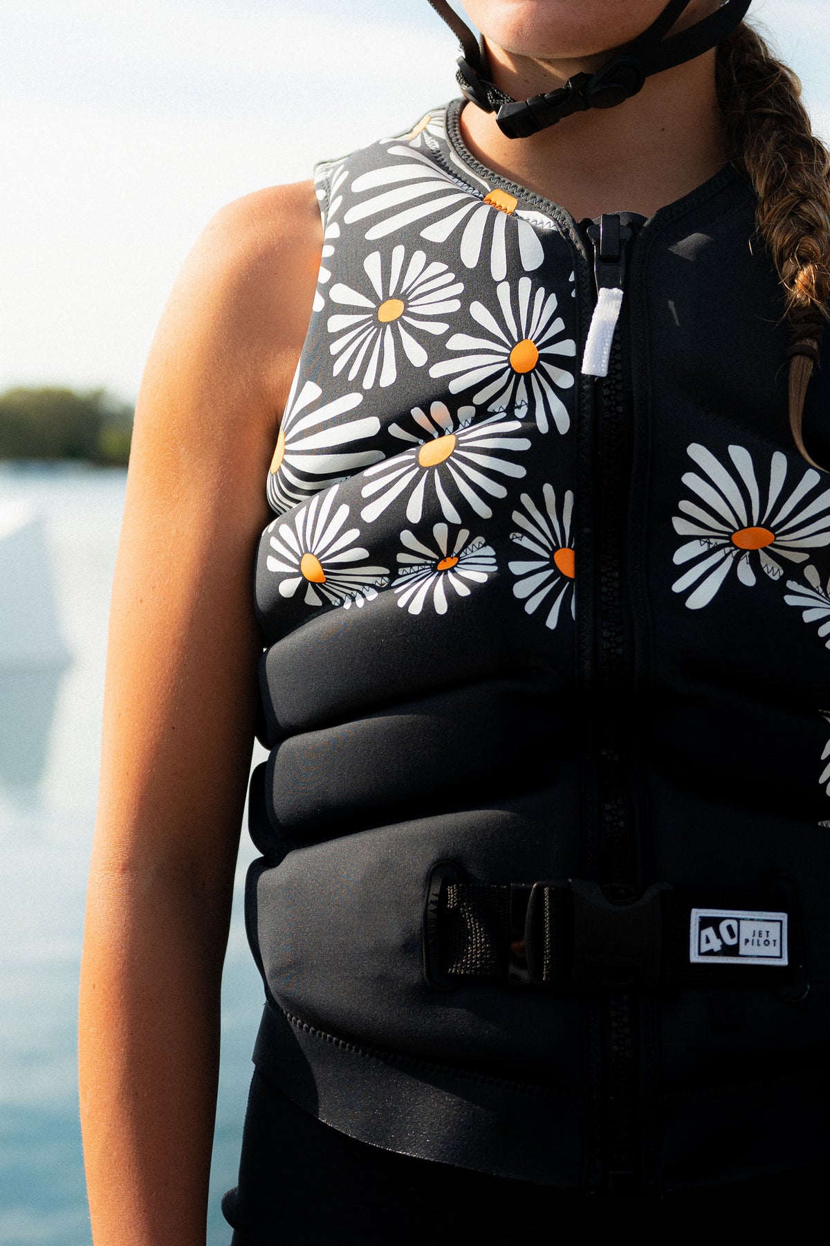 Rider in a helmet wearing the Charcoal Isla life jacket by the water, with daisies across the chest