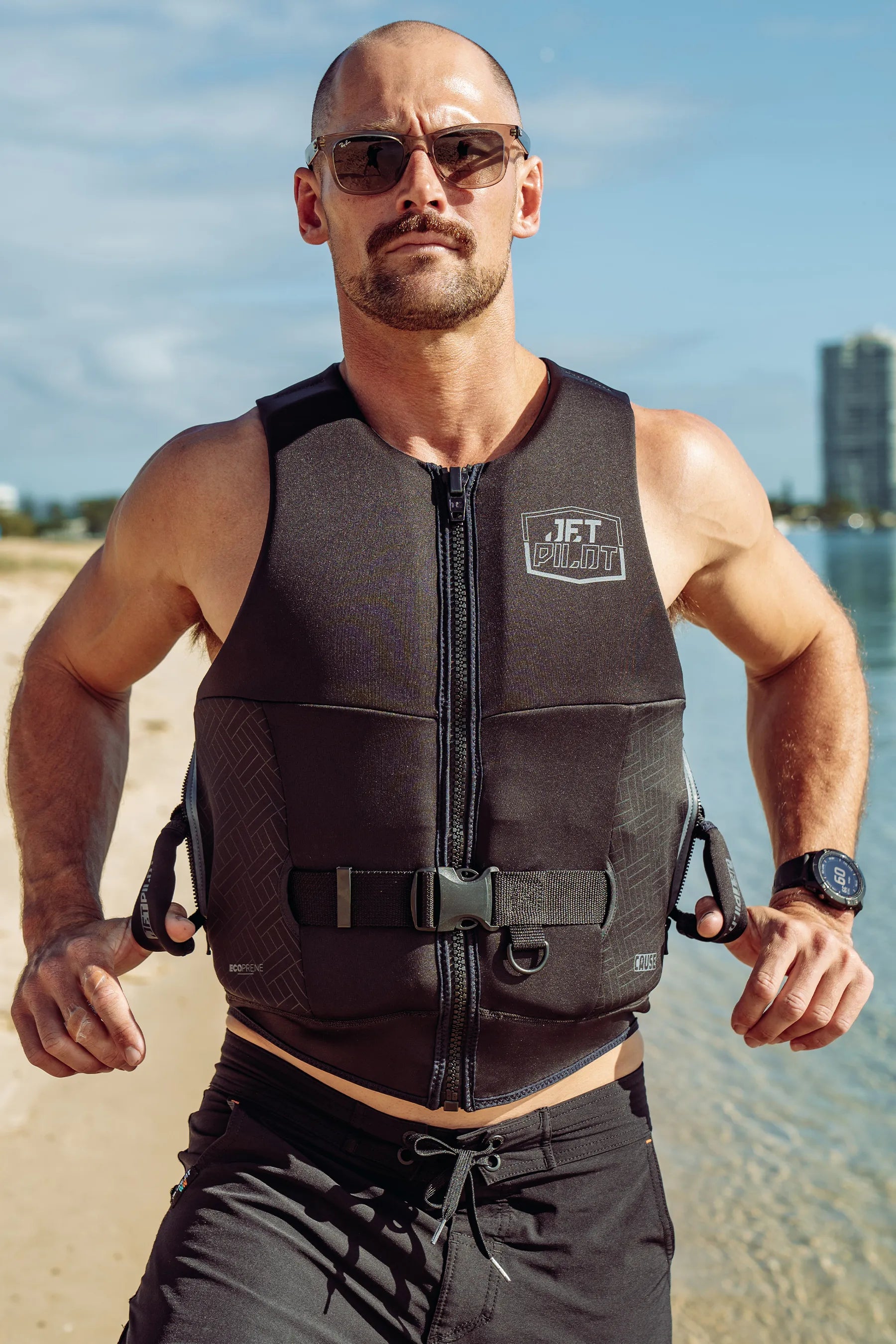 Man wearing a Jetpilot Cause Life Jacket - Black with a logo on a beach