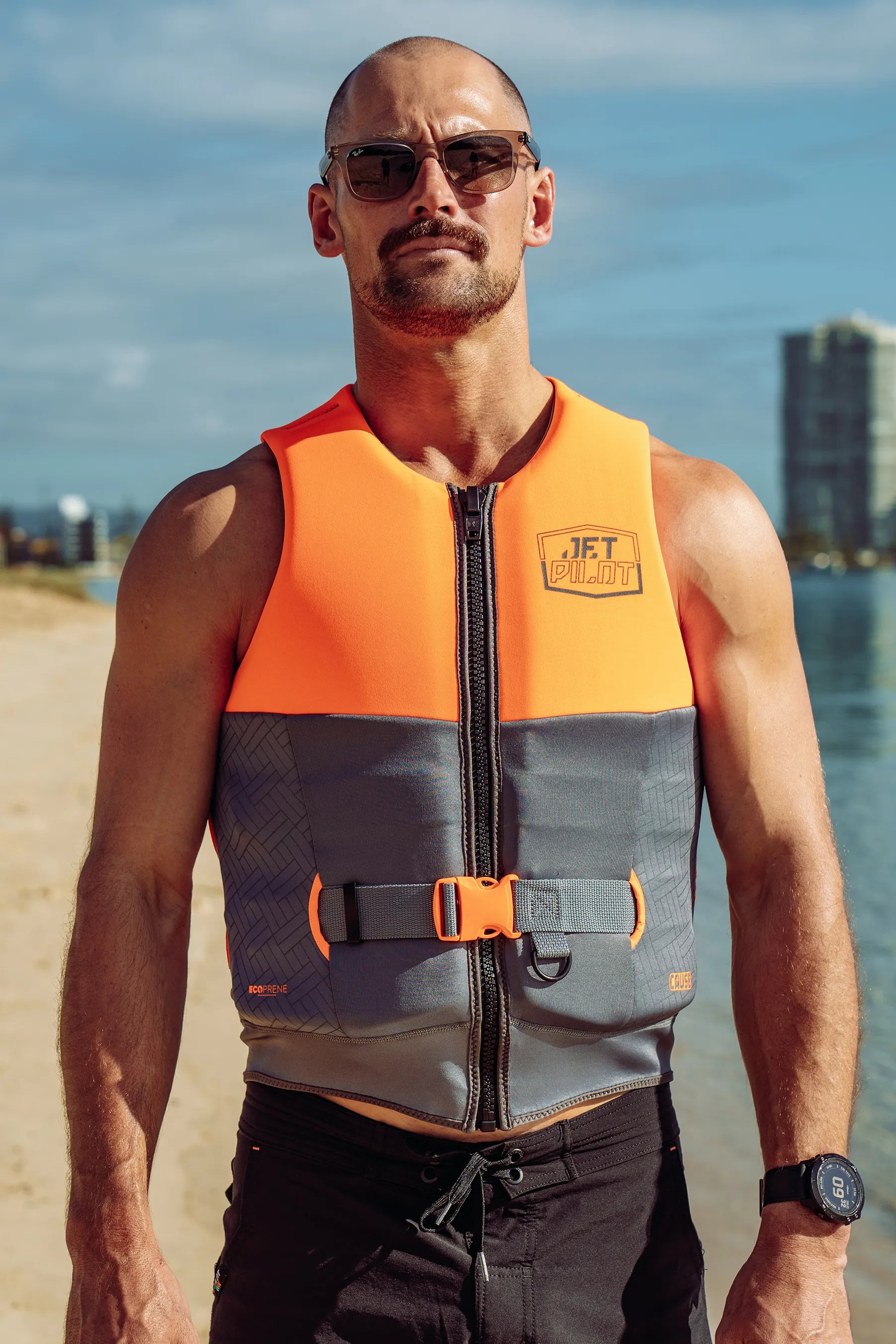 Man wearing an Jetpilot Cause Life Jacket - Charcoal/Orange L50 with a river and cityscape in the background