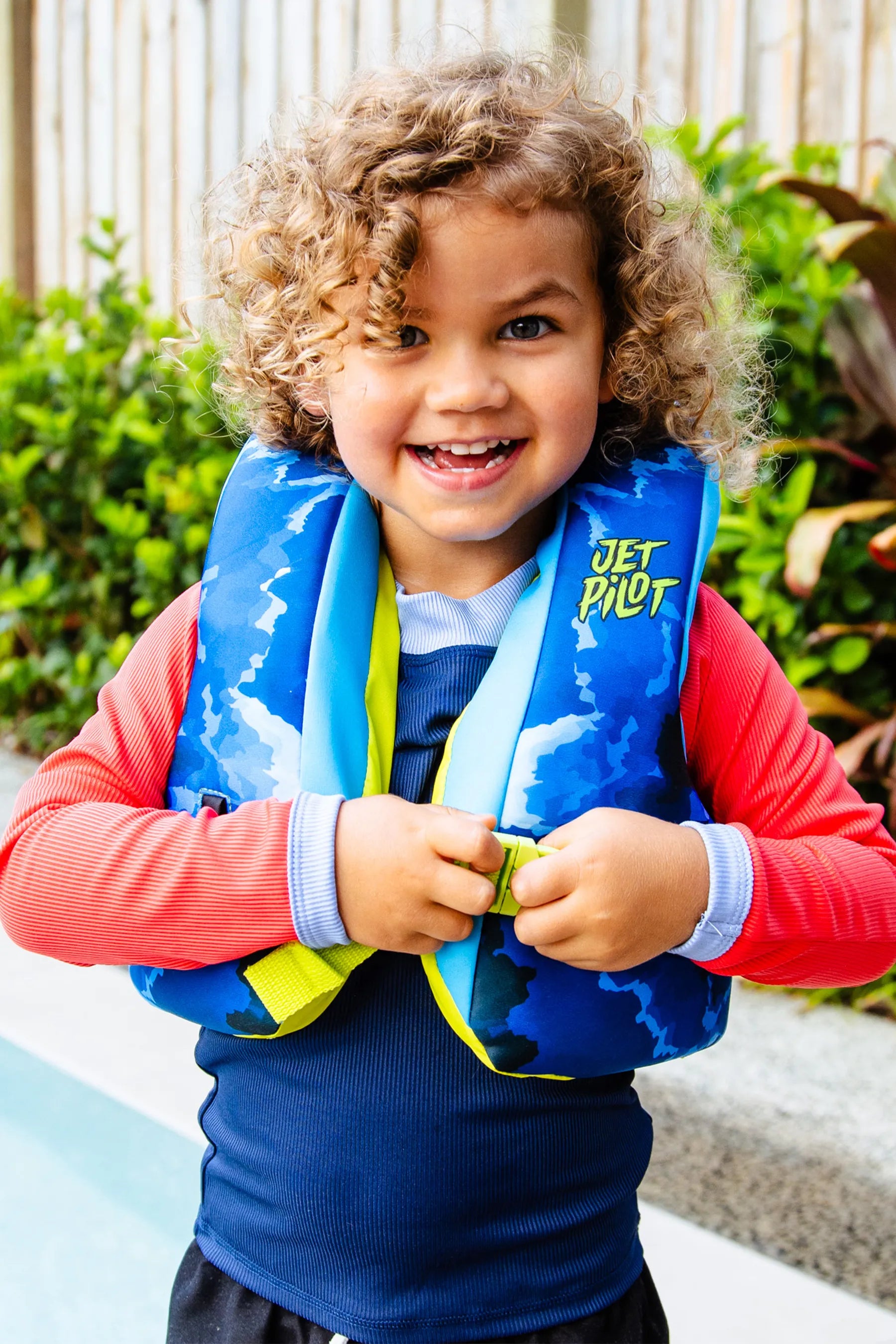 Child wearing a blue Jetpilot Paddle Pal Splash Swim Vest - Blue with 'Jetpilot' branding outdoors.