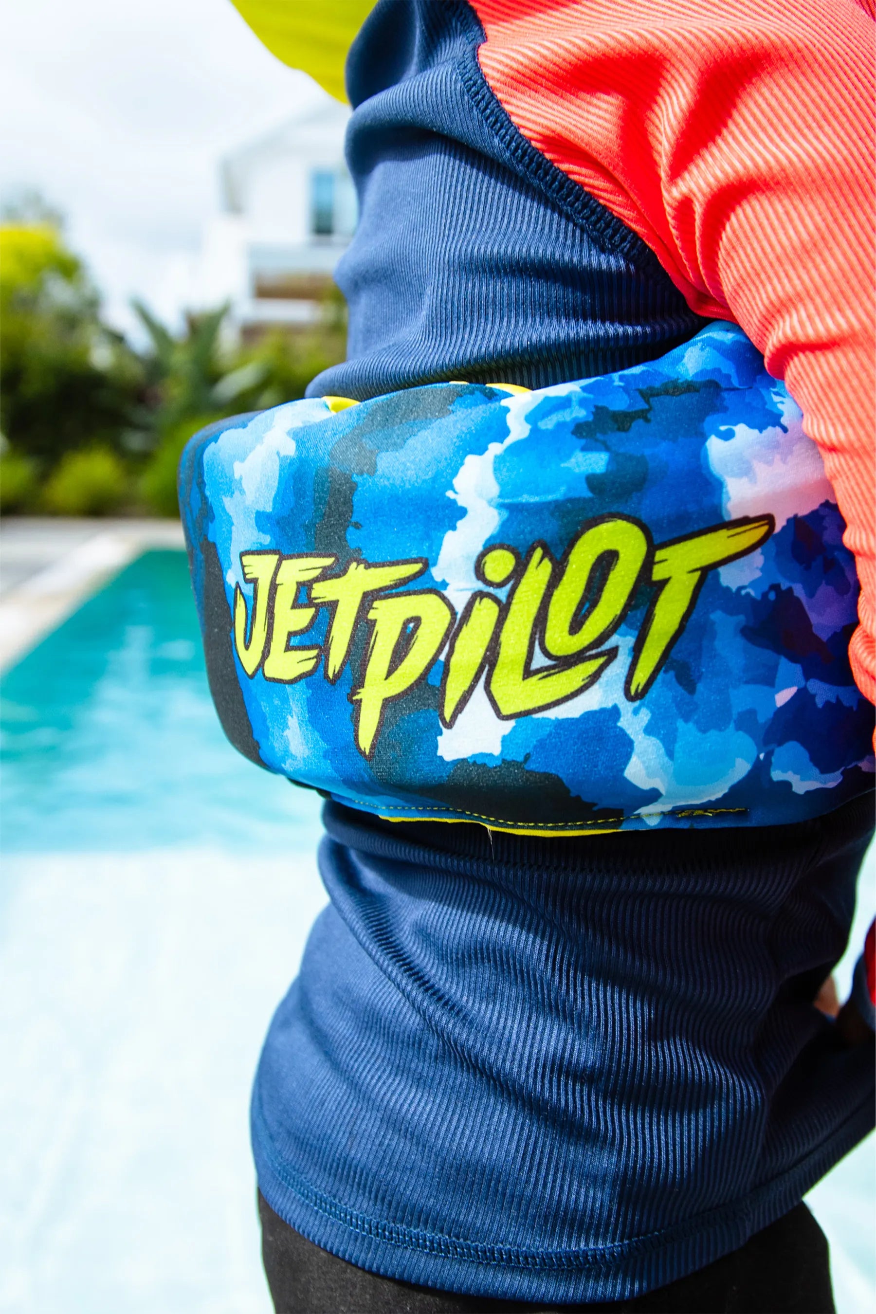 Child wearing Jetpilot Paddle Pal Splash Swim Vest - Blue with 'JETPILOT' branding held by a pool.