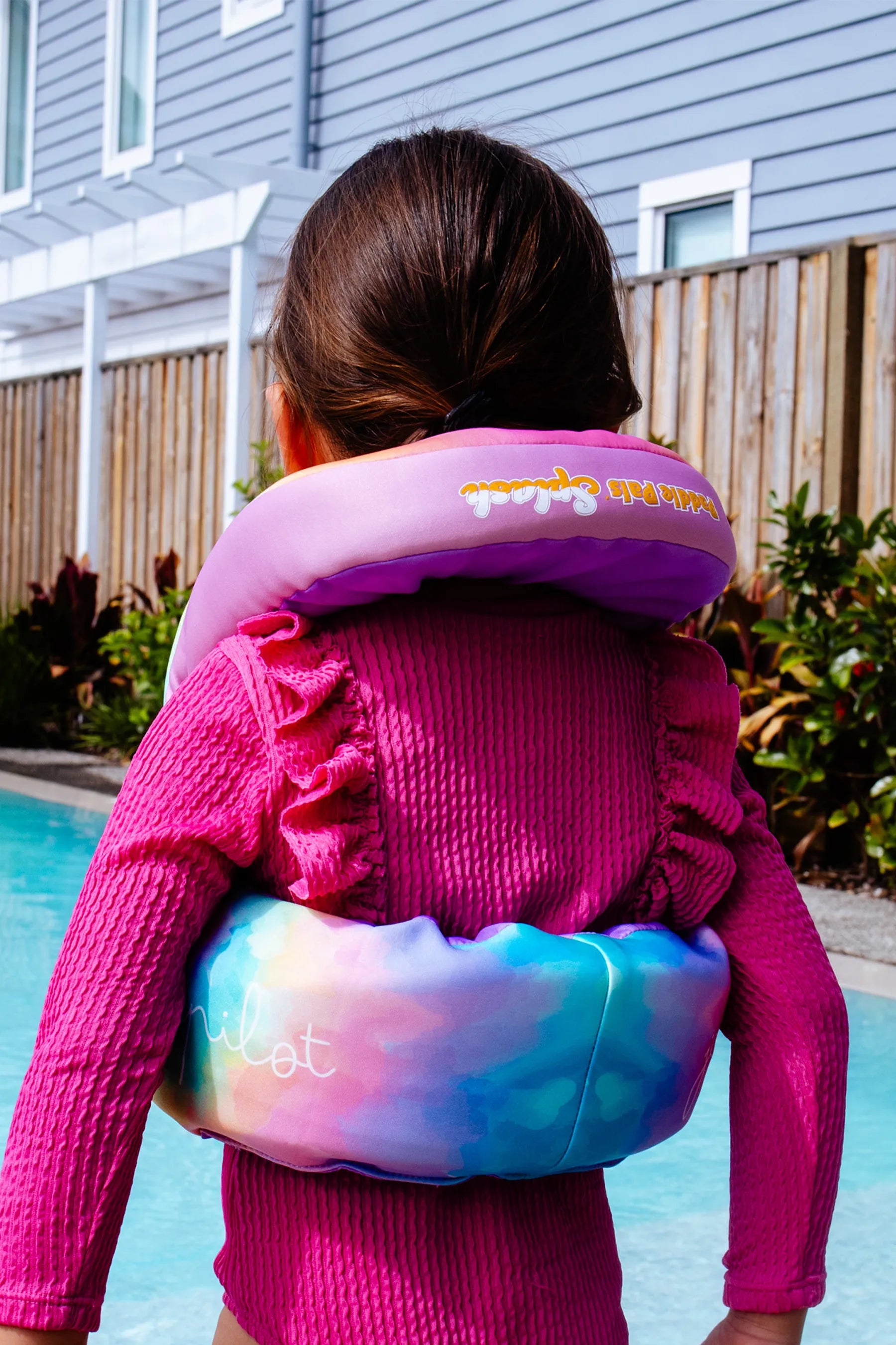 Child wearing a Jetpilot Paddle Pal Splash Swim Vest - Tie Dye with a pool in the background