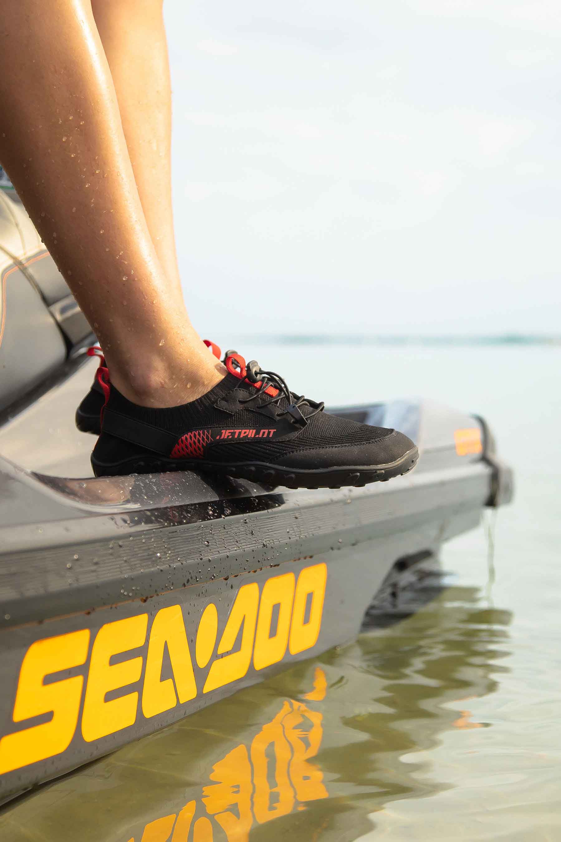 Person wearing black shoes stepping onto a Sea-Doo watercraft in shallow water.