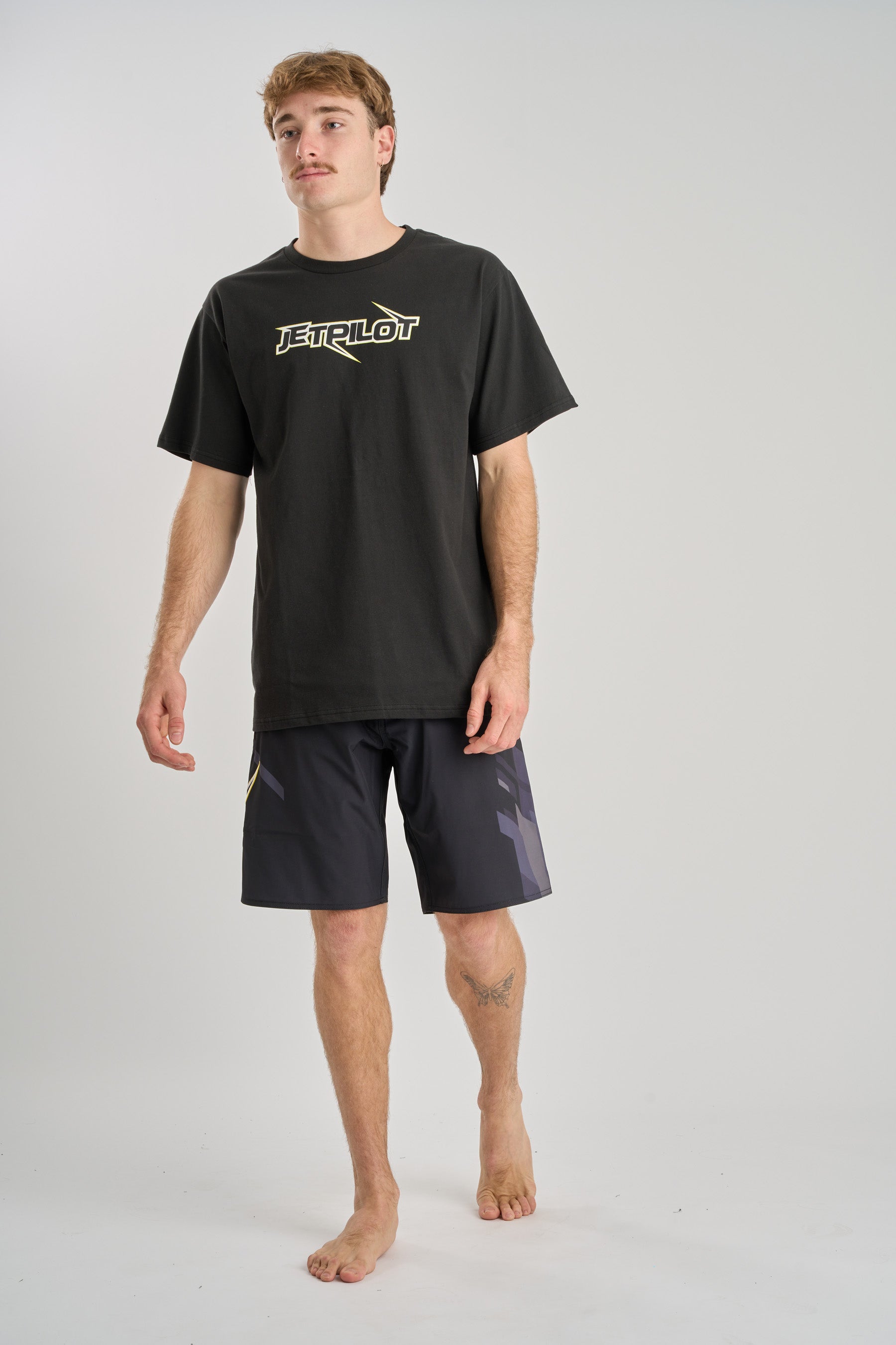 Man wearing a black t-shirt with a logo and black shorts on a light gray background