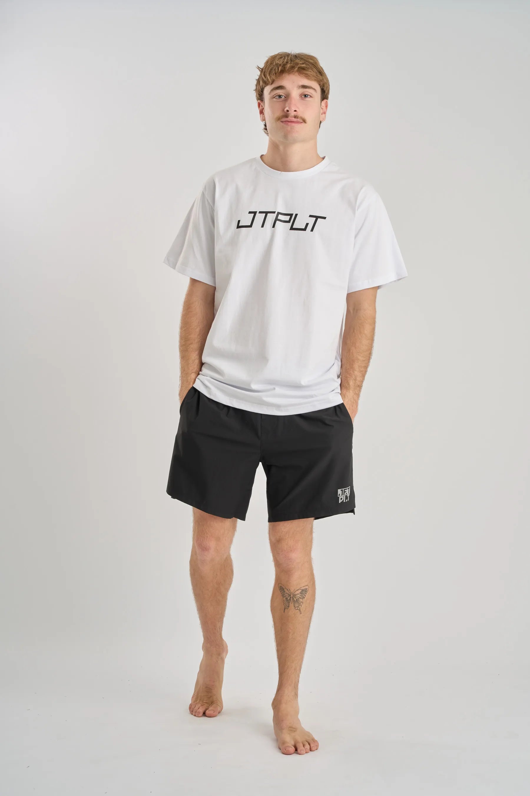 Person wearing a white t-shirt and black shorts with branding on a plain background — image 2