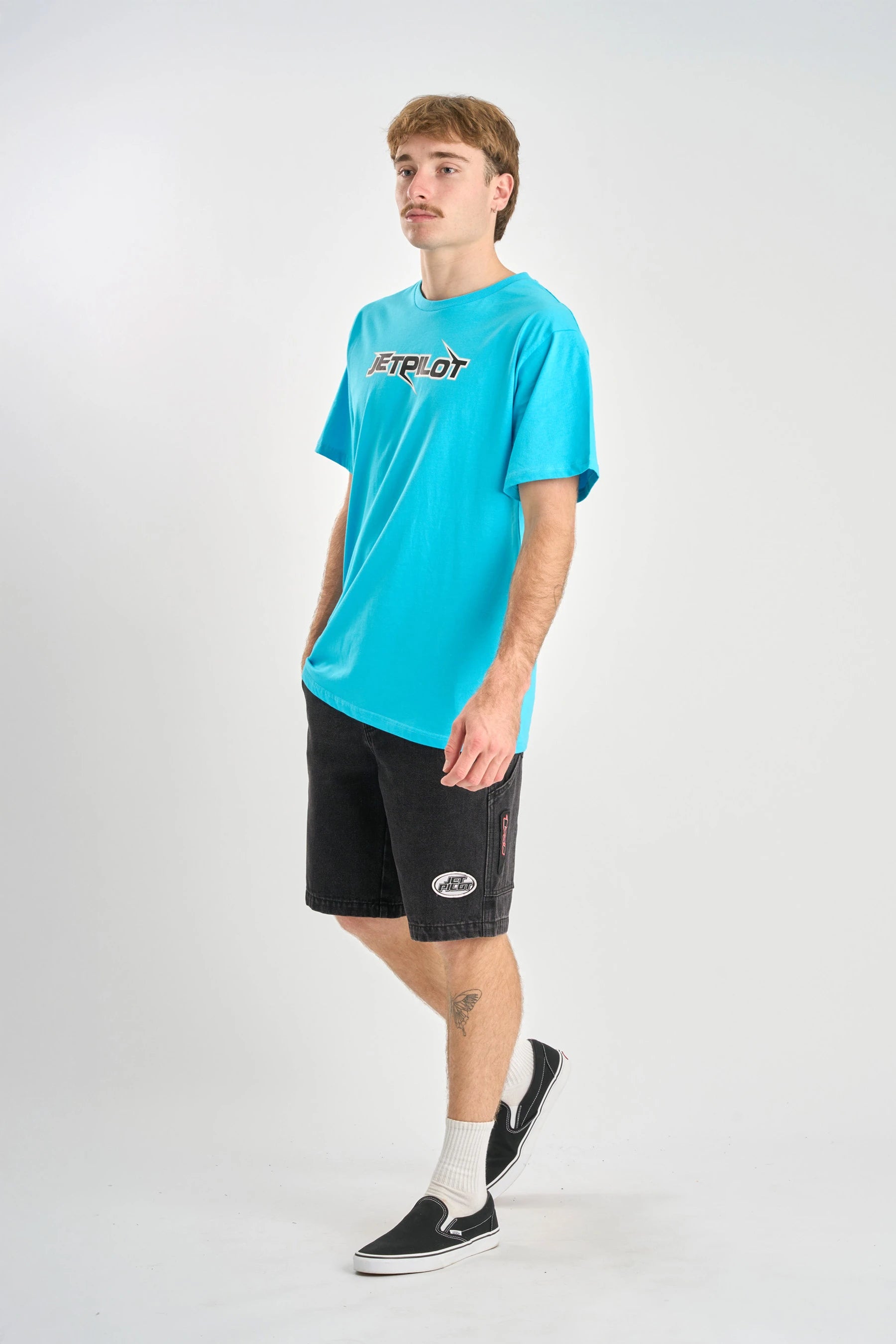 Person wearing a turquoise t-shirt with a logo and black shorts on a white background — image 2