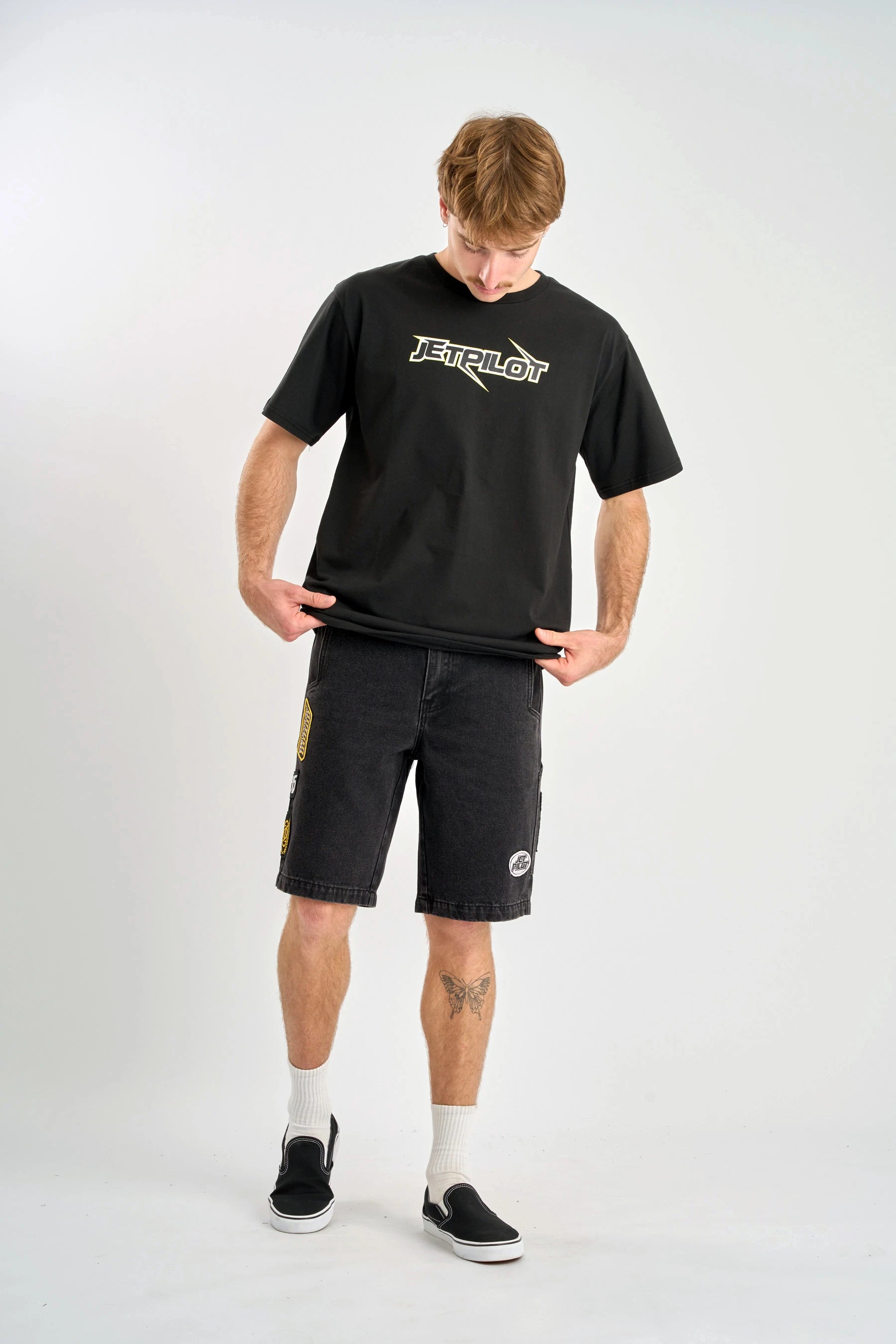 Person wearing a black t-shirt with a logo and black shorts on a white background — image 4