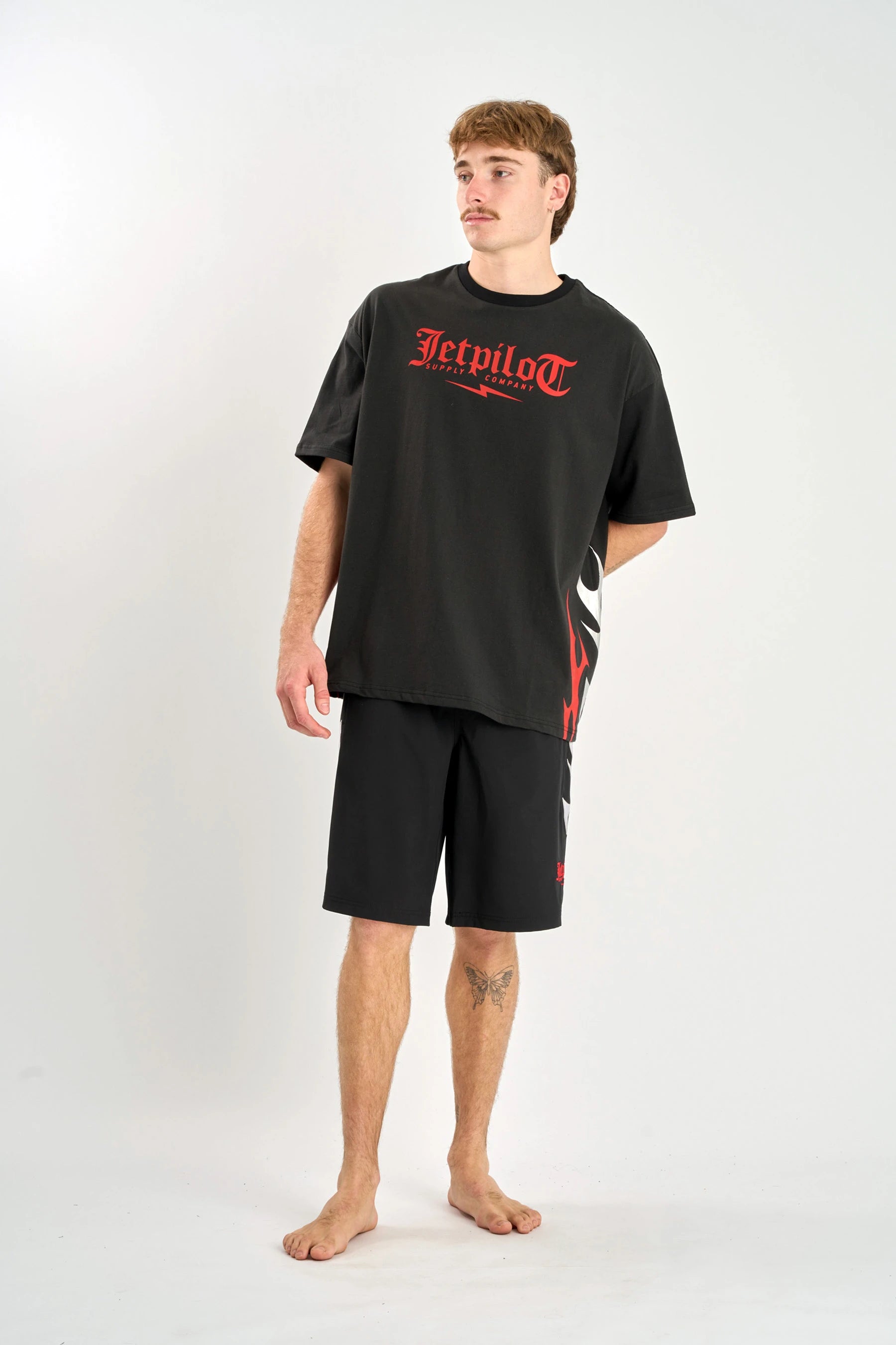 Person wearing a Jetpilot Tribal Heavy Tee - Black with red text and black shorts on a white background — image 2