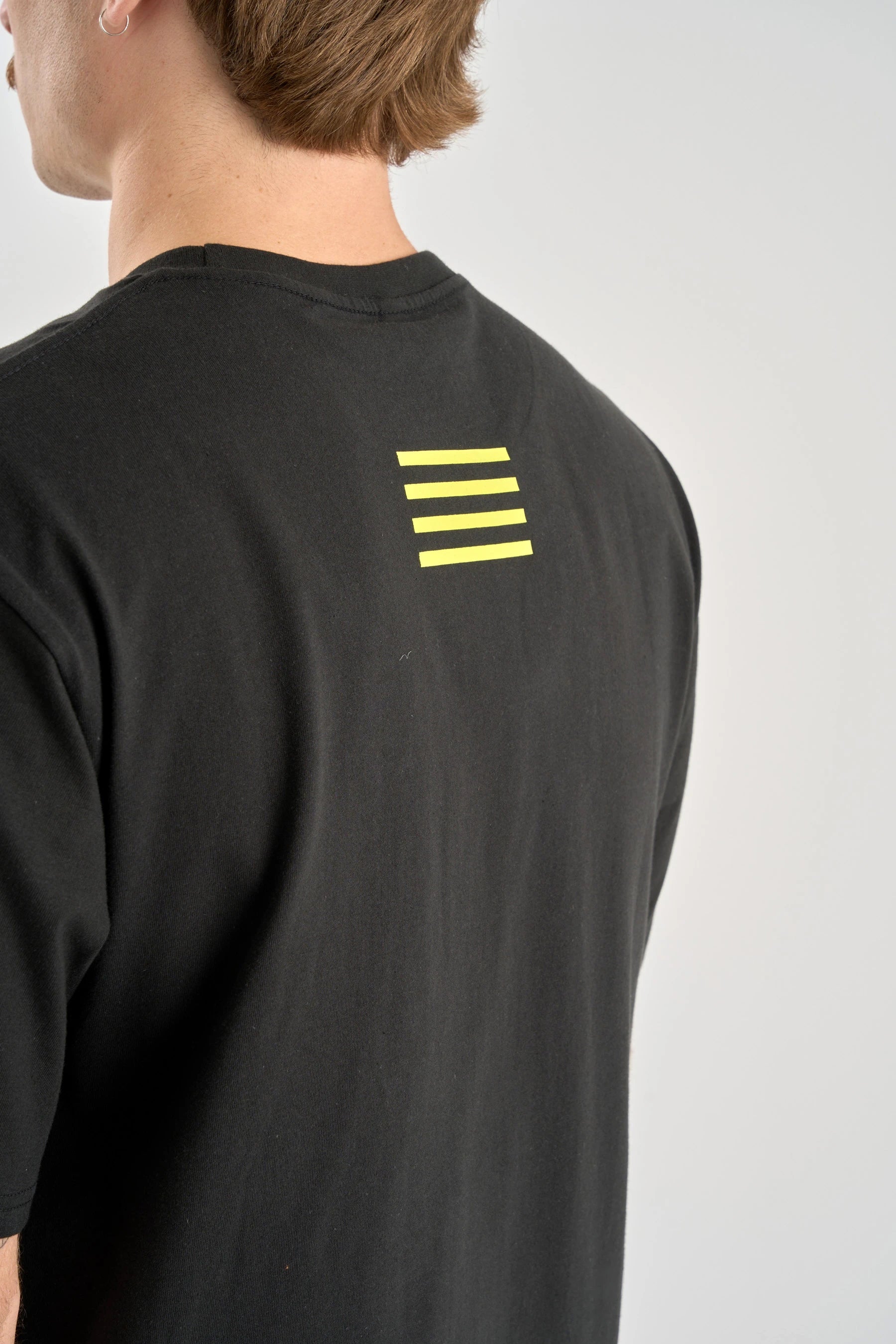 Person wearing a Jetpilot Vault SS Tee - Black shirt with yellow stripes on the back against a white background — image 2