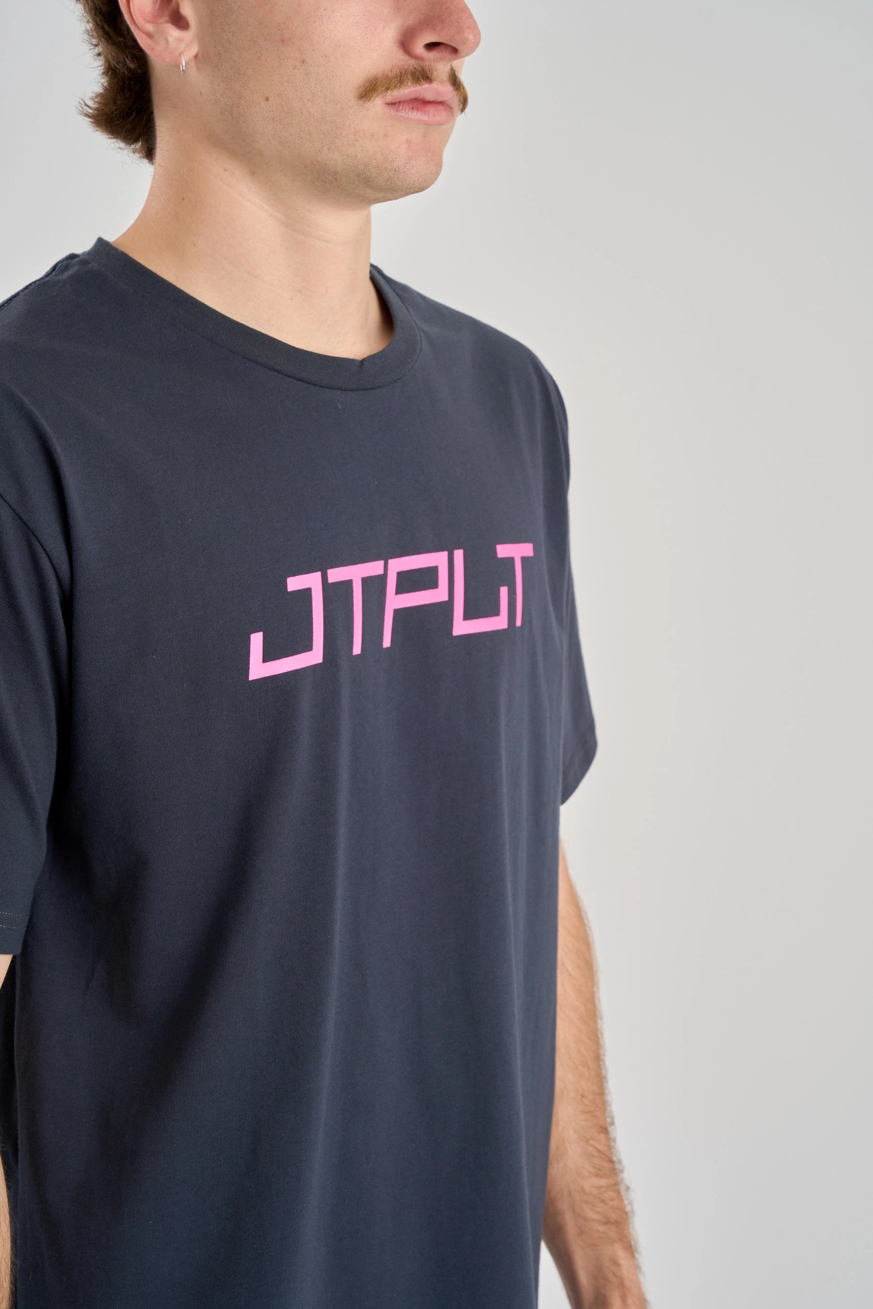 Person wearing a navy t-shirt with pink logo on a plain background — image 2