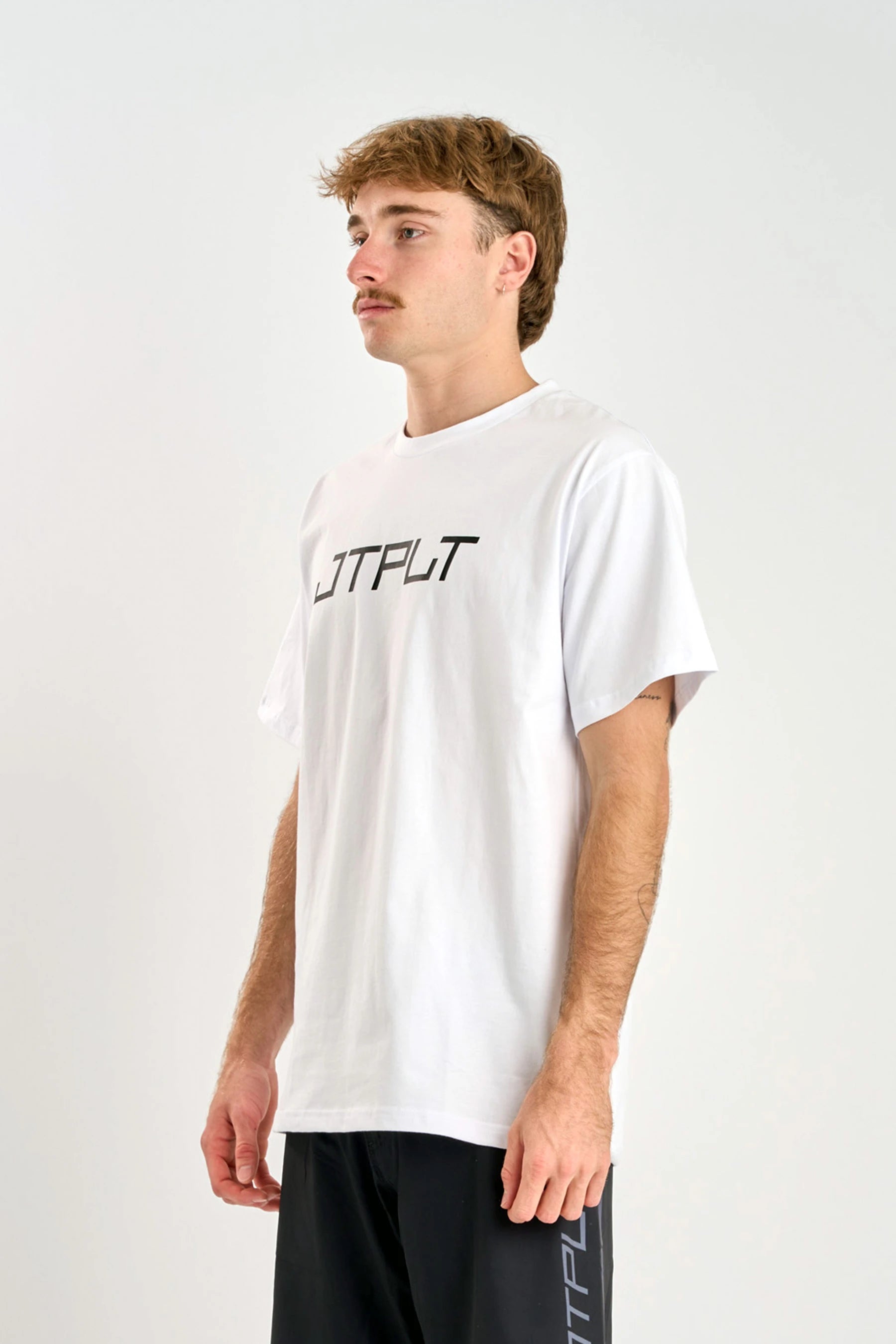 Person wearing a white t-shirt with 'JTPLT' text on a plain background — image 2