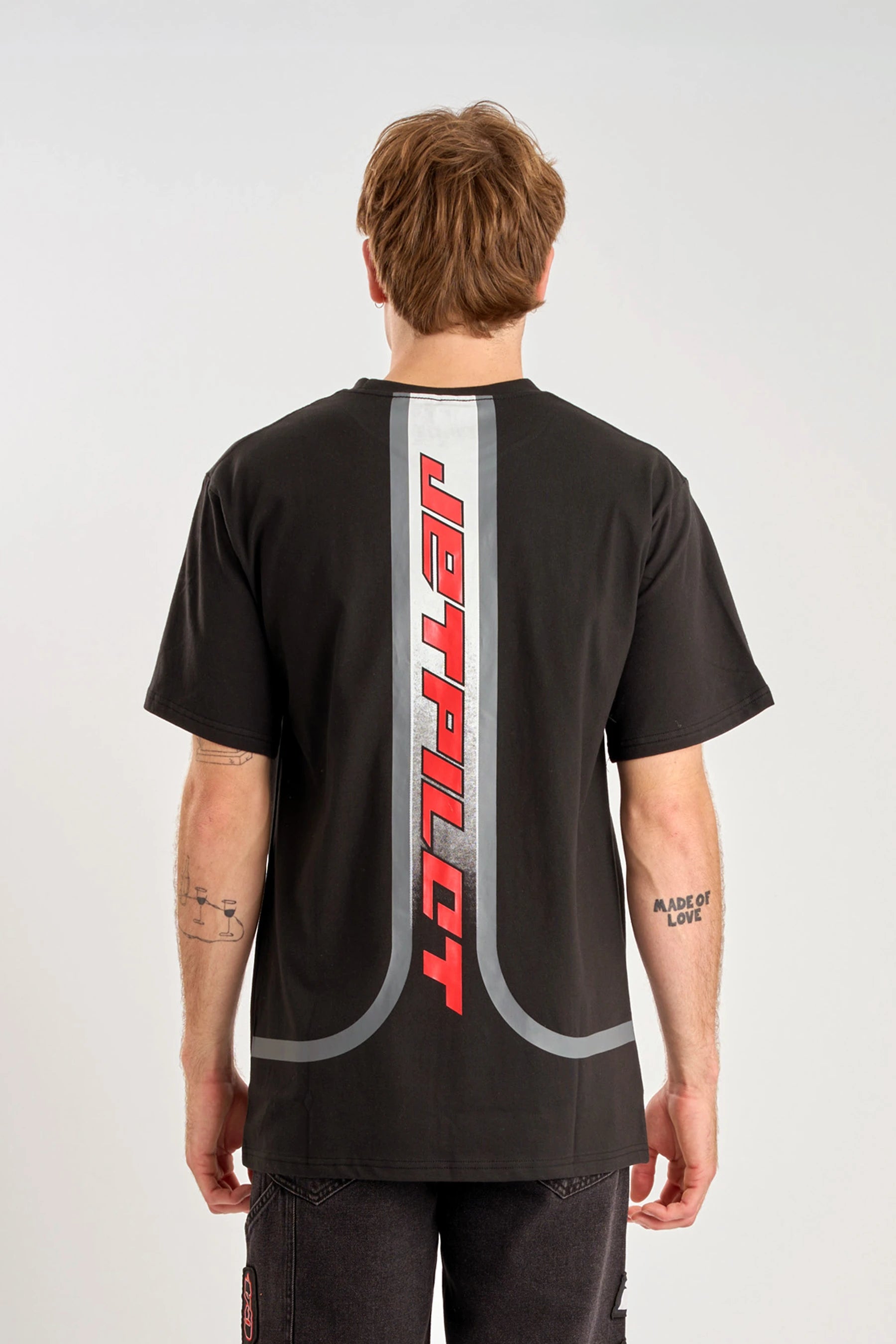 Person wearing a black t-shirt with Red 'Jetpilot' logo on a gradient graphic design on back against a white background — ima