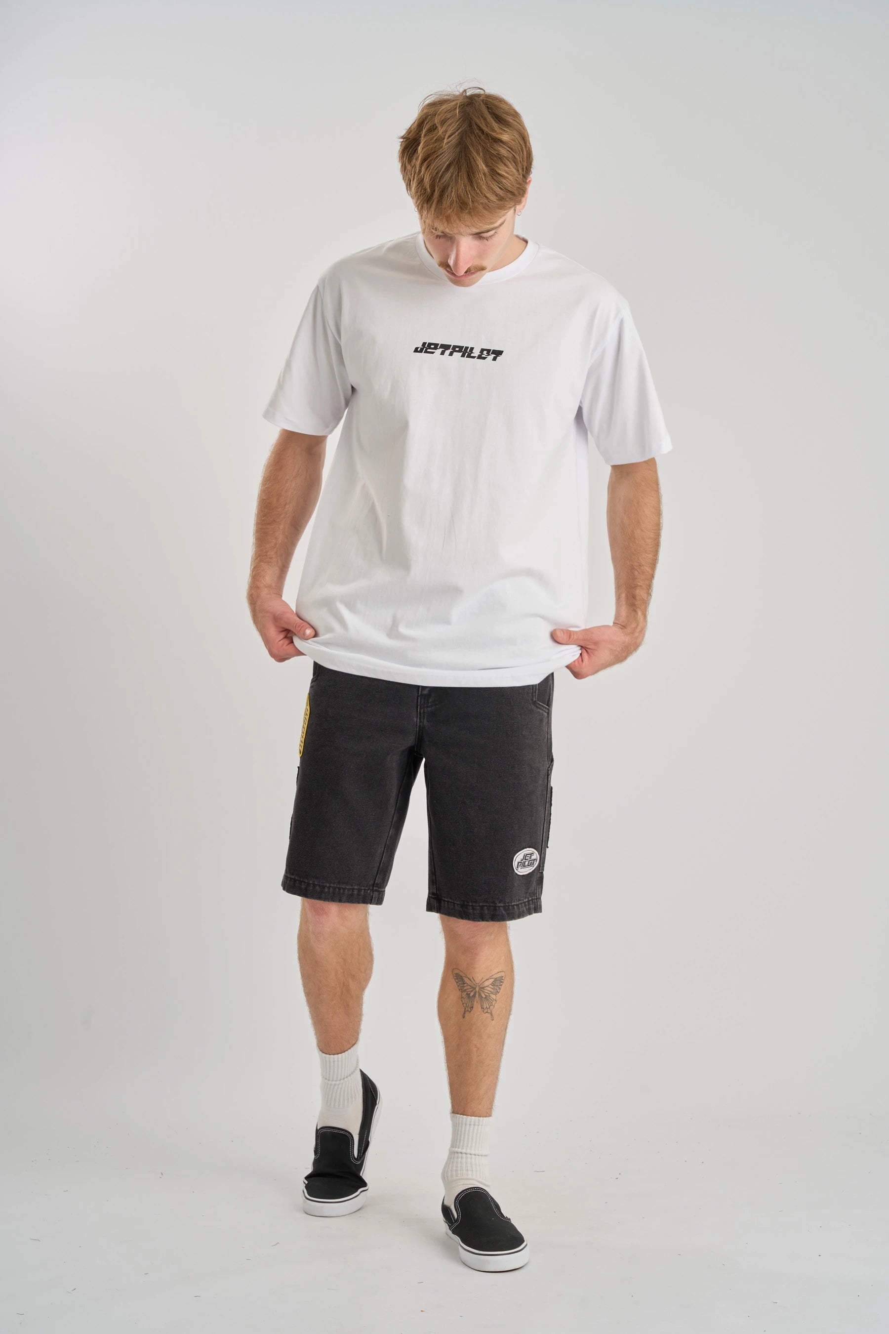 Person wearing a white Jetpilot t-shirt and black shorts on a plain background — image 2