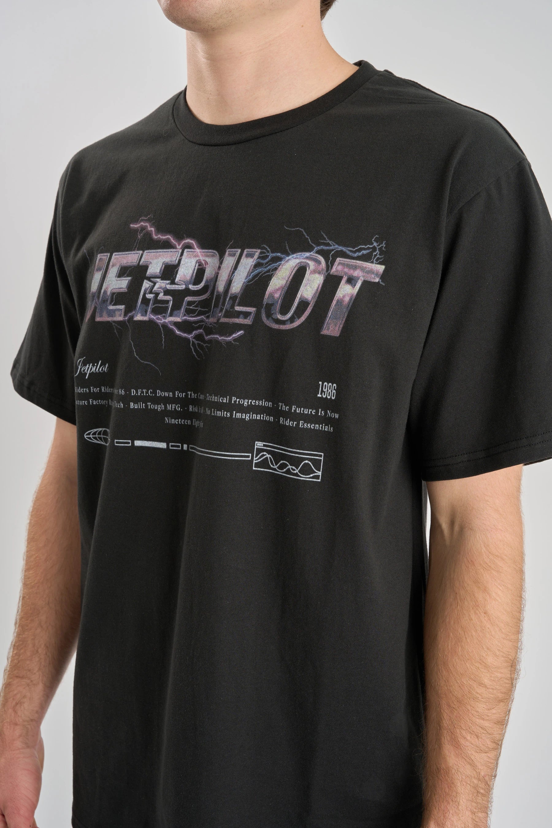 Close Up of a Person wearing a Jetpilot t-shirt with lightning graphic design on a plain background