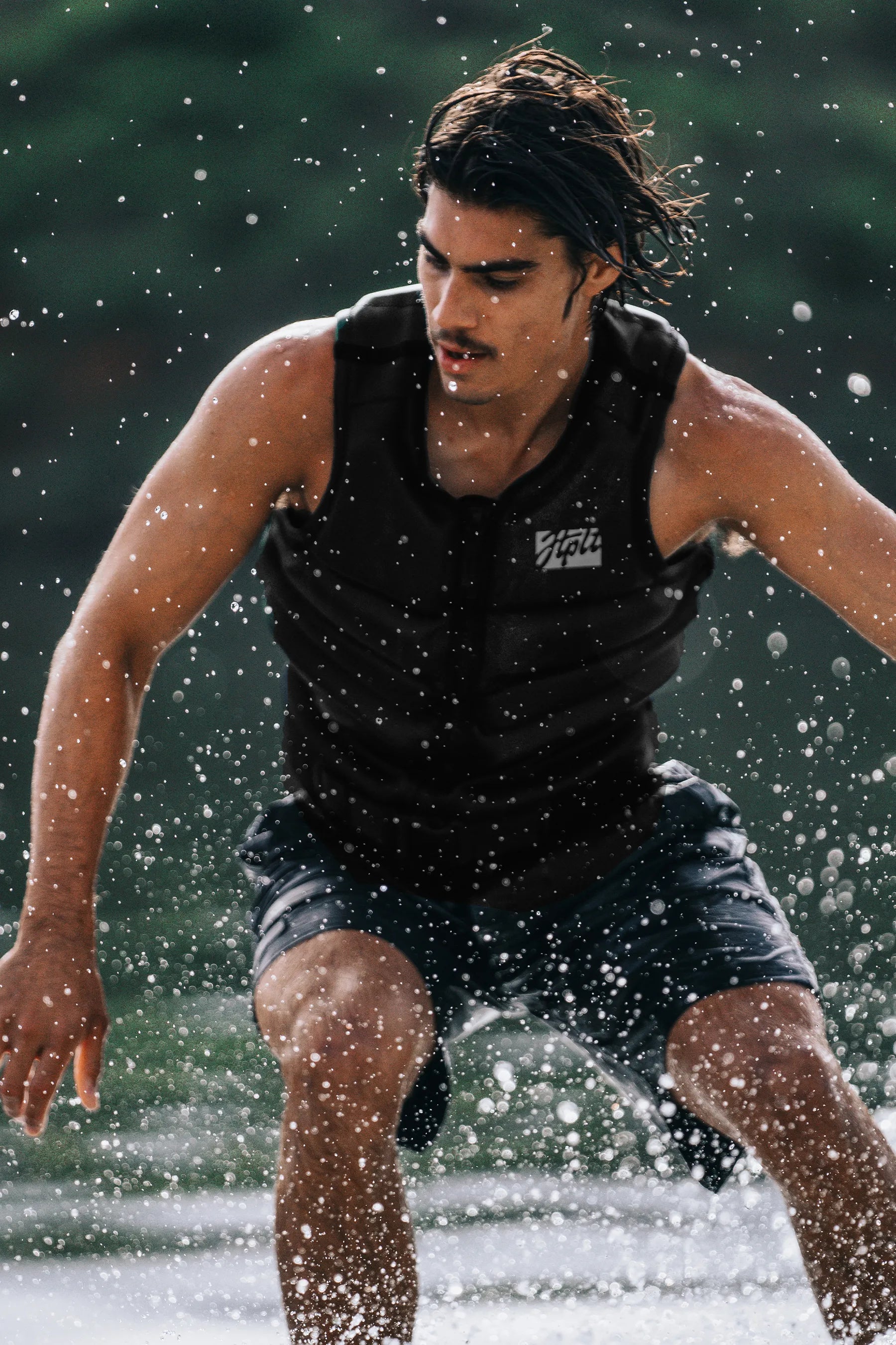 Person wakesurfing, wearing Jetpilot Phase Hyperflex Life Jacket - Black with branding.