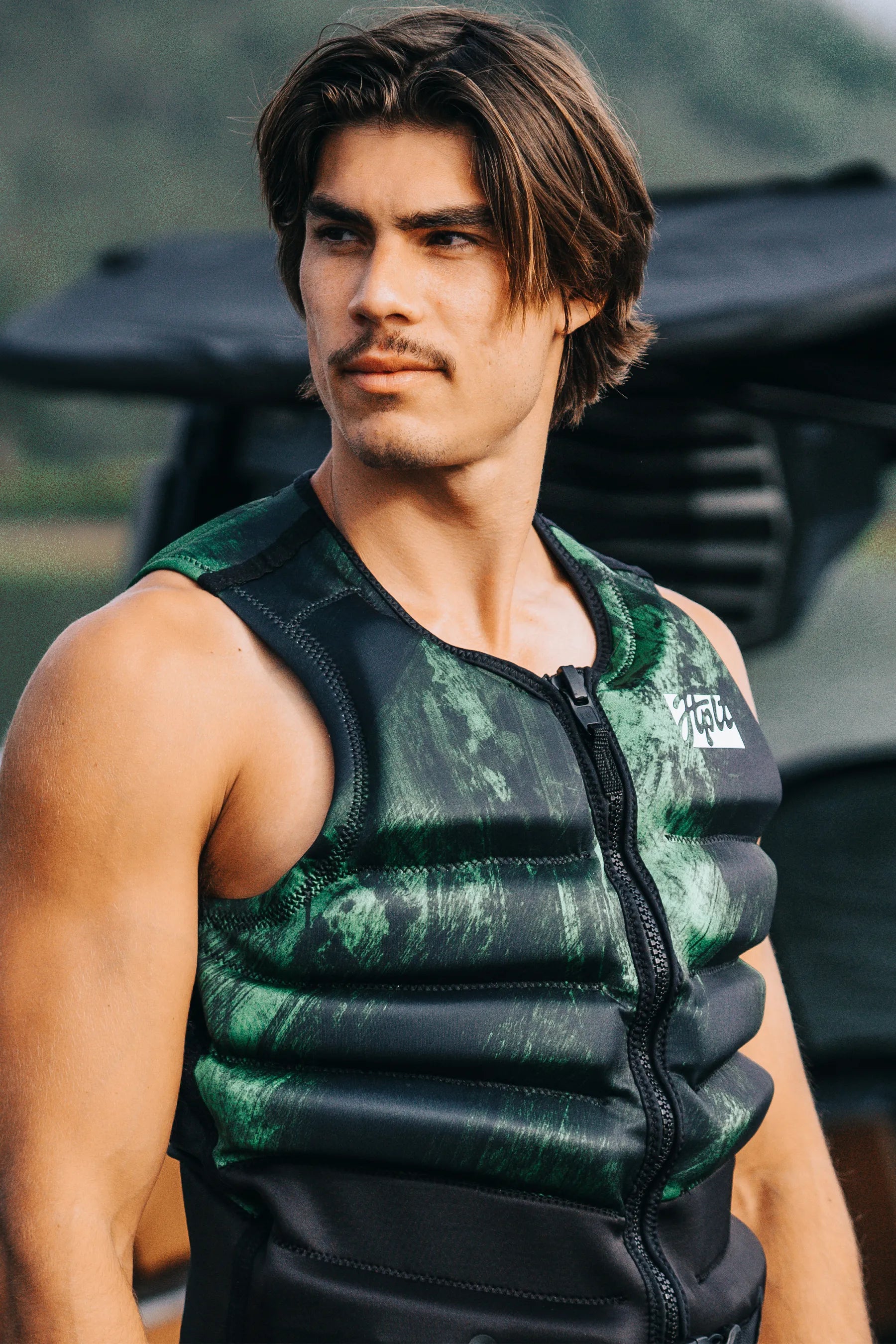 Man wearing a green and black life vest with a blurred background