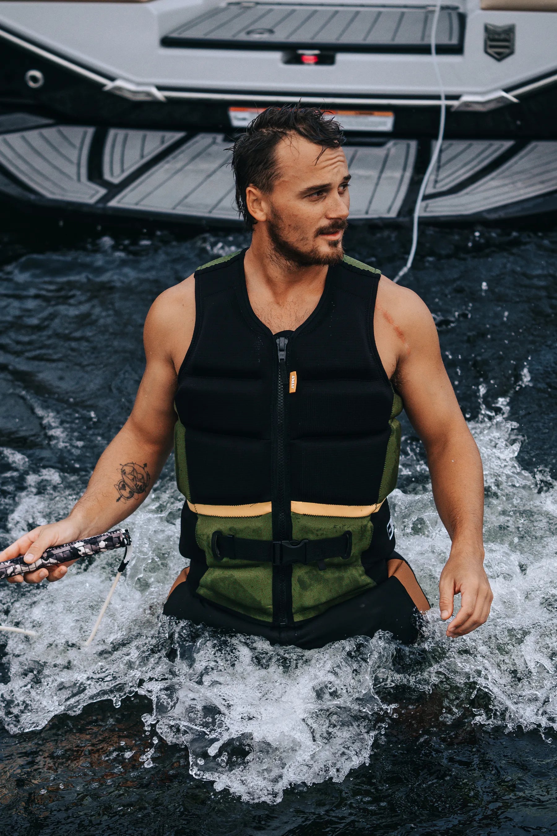Man in aJetpilot Pro C4 Life Jacket - Cory Tuenissen Signature Series - Black/Sage  standing in water near a boat