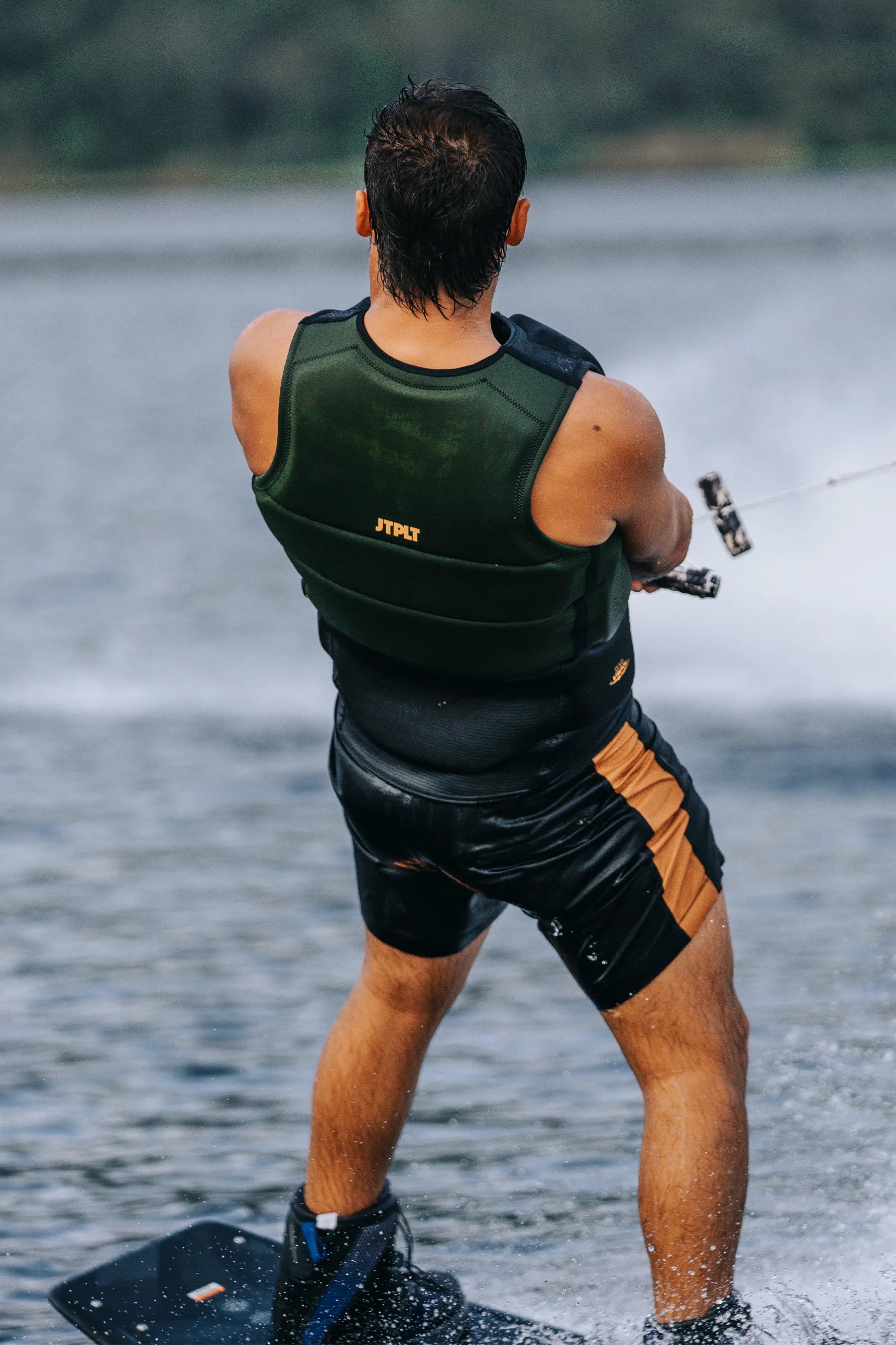 Person water skiing wearing a Jetpilot Pro C4 Life Jacket - Cory Tuenissen Signature Series - Black/Sage and black shorts on a lake.