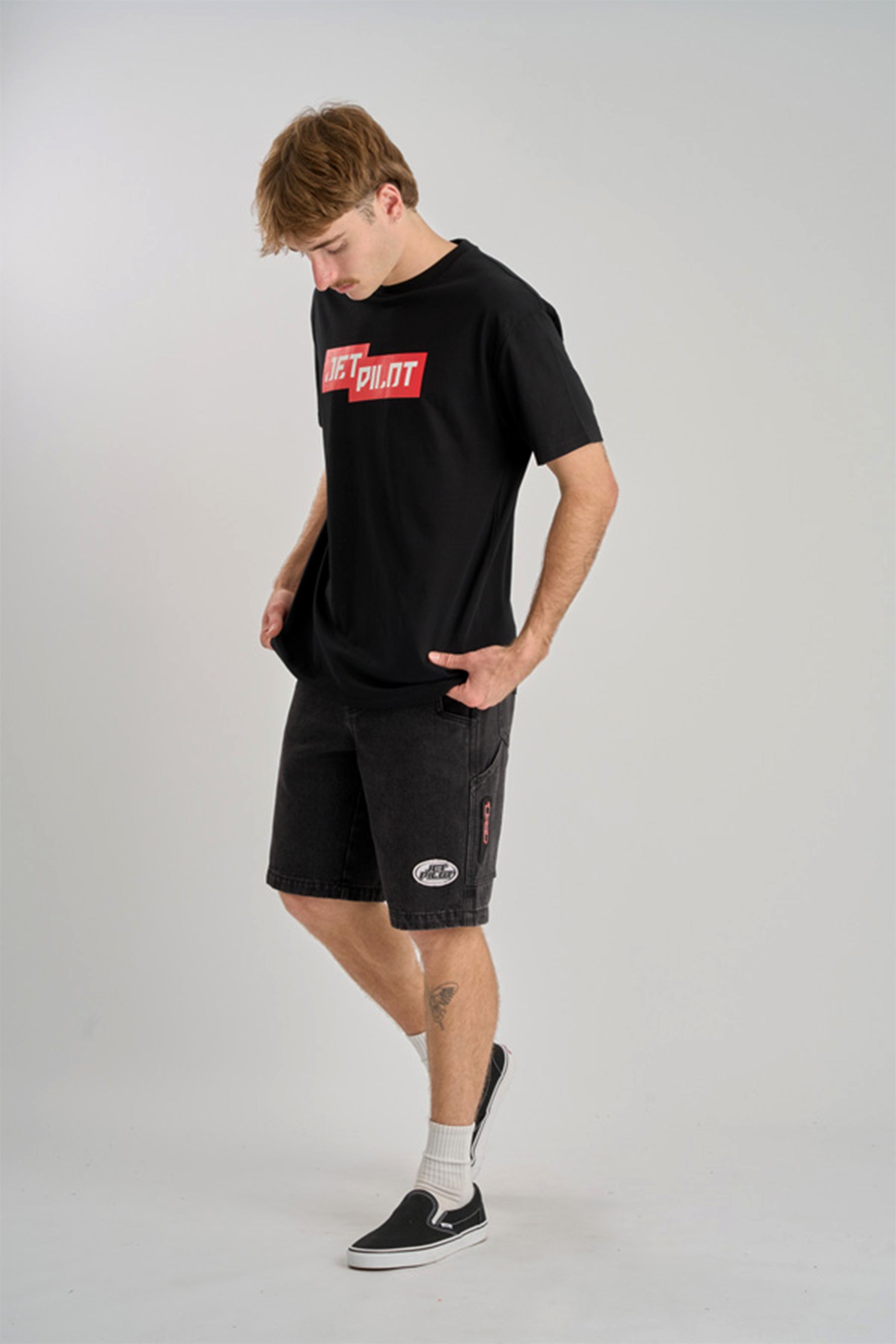 Man wearing a black t-shirt with a red logo and black shorts on a gray background