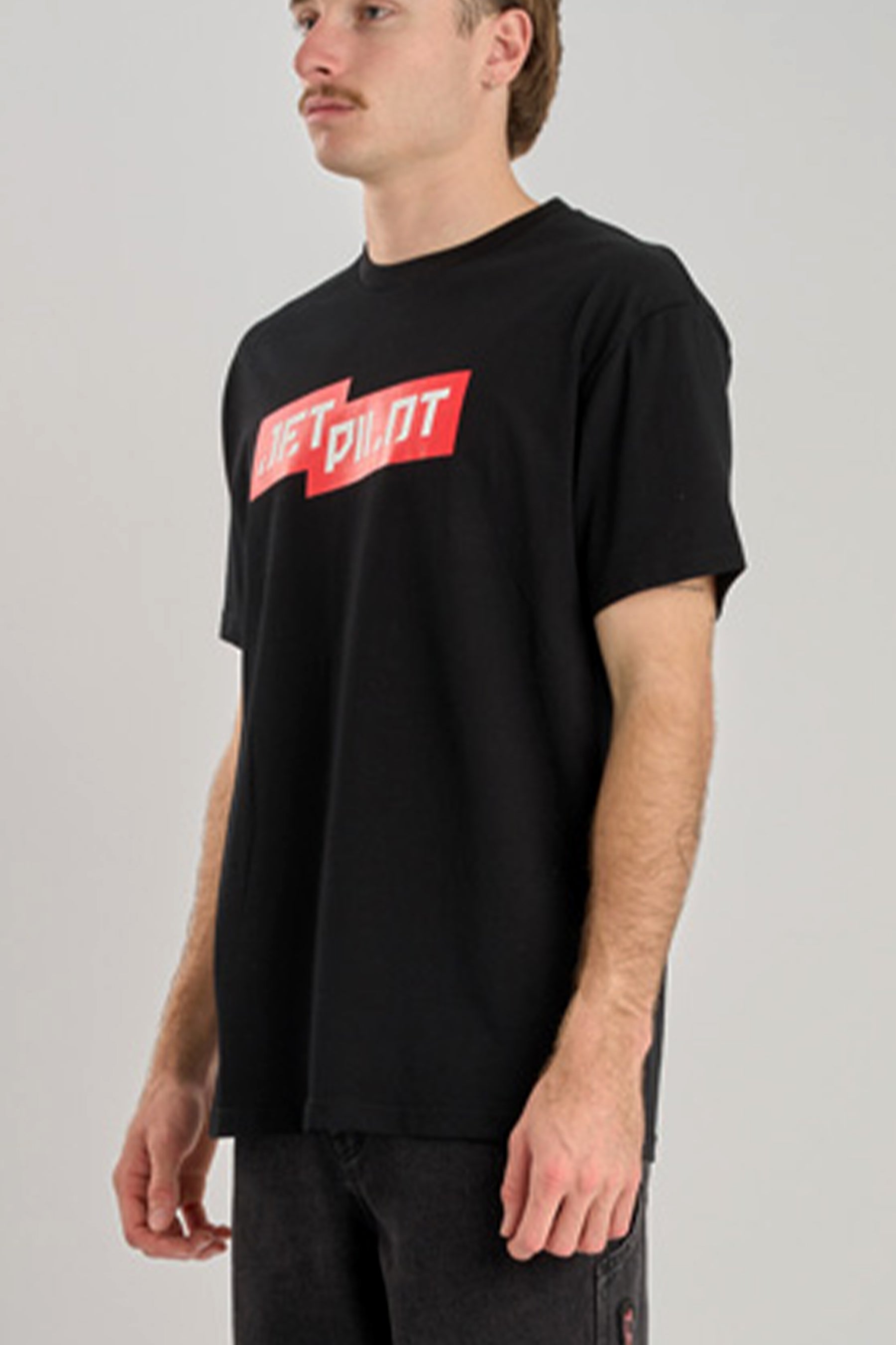 Person wearing a black t-shirt with a red and white logo on a plain background