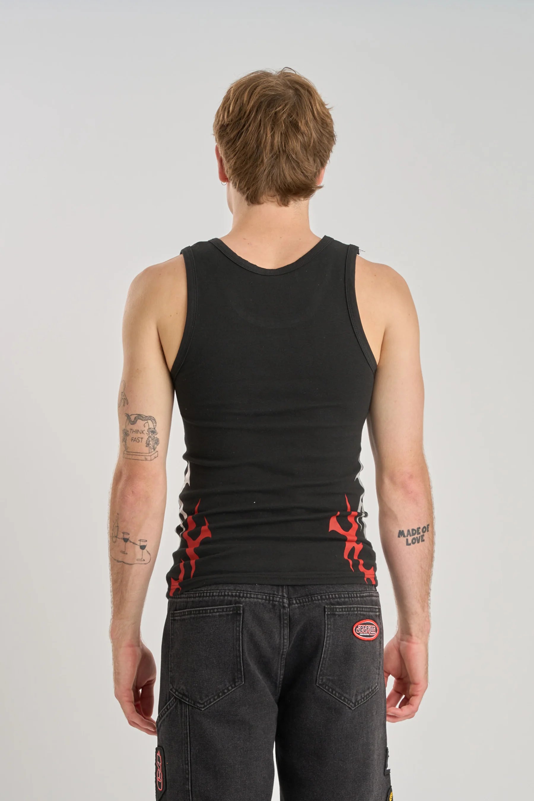 Person wearing a black tank top with red designs on a plain background