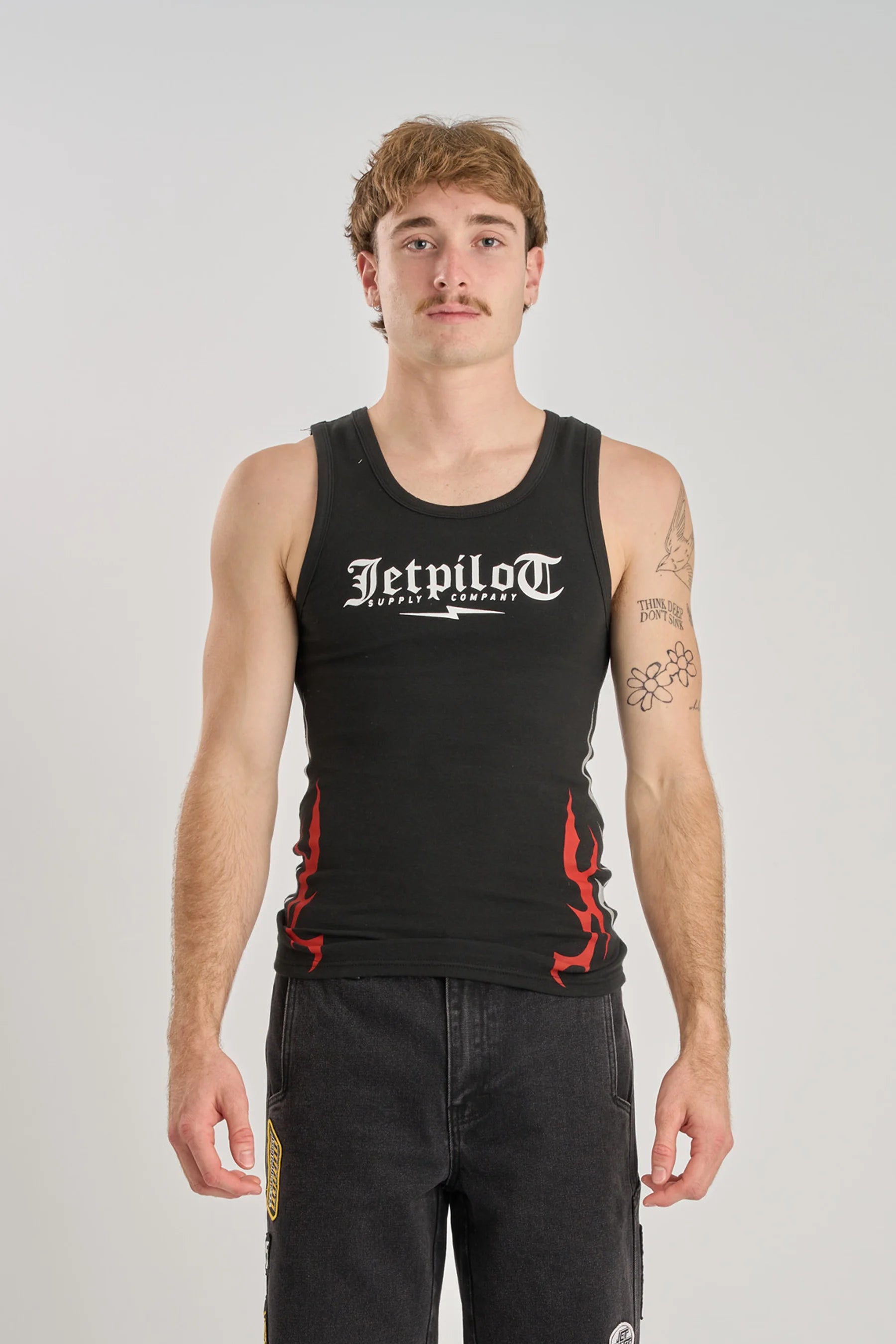 Person wearing a Jetpilot Tribal Singlet - Black with white text and red designs on a plain background