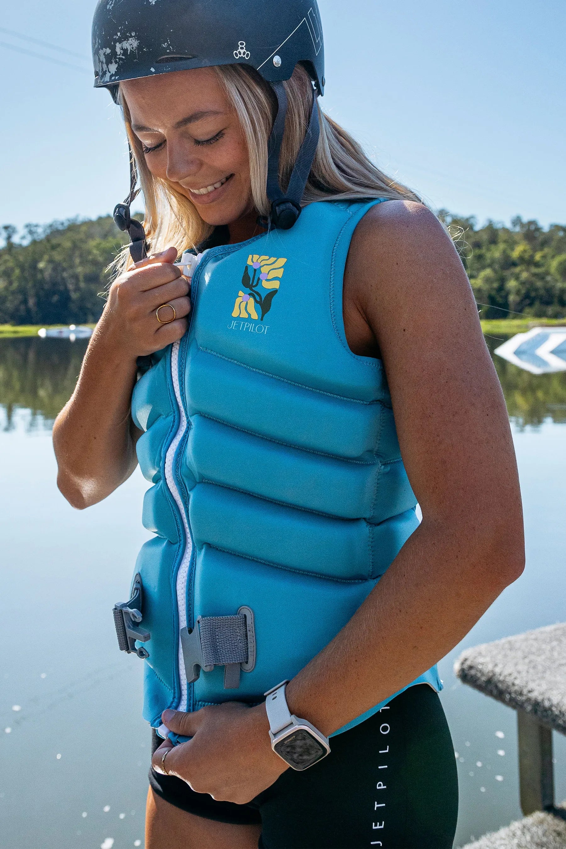 Person wearing a Jetpilot X1 Ladies Life Jacket - Luna - Blue life jacket and helmet by a body of water