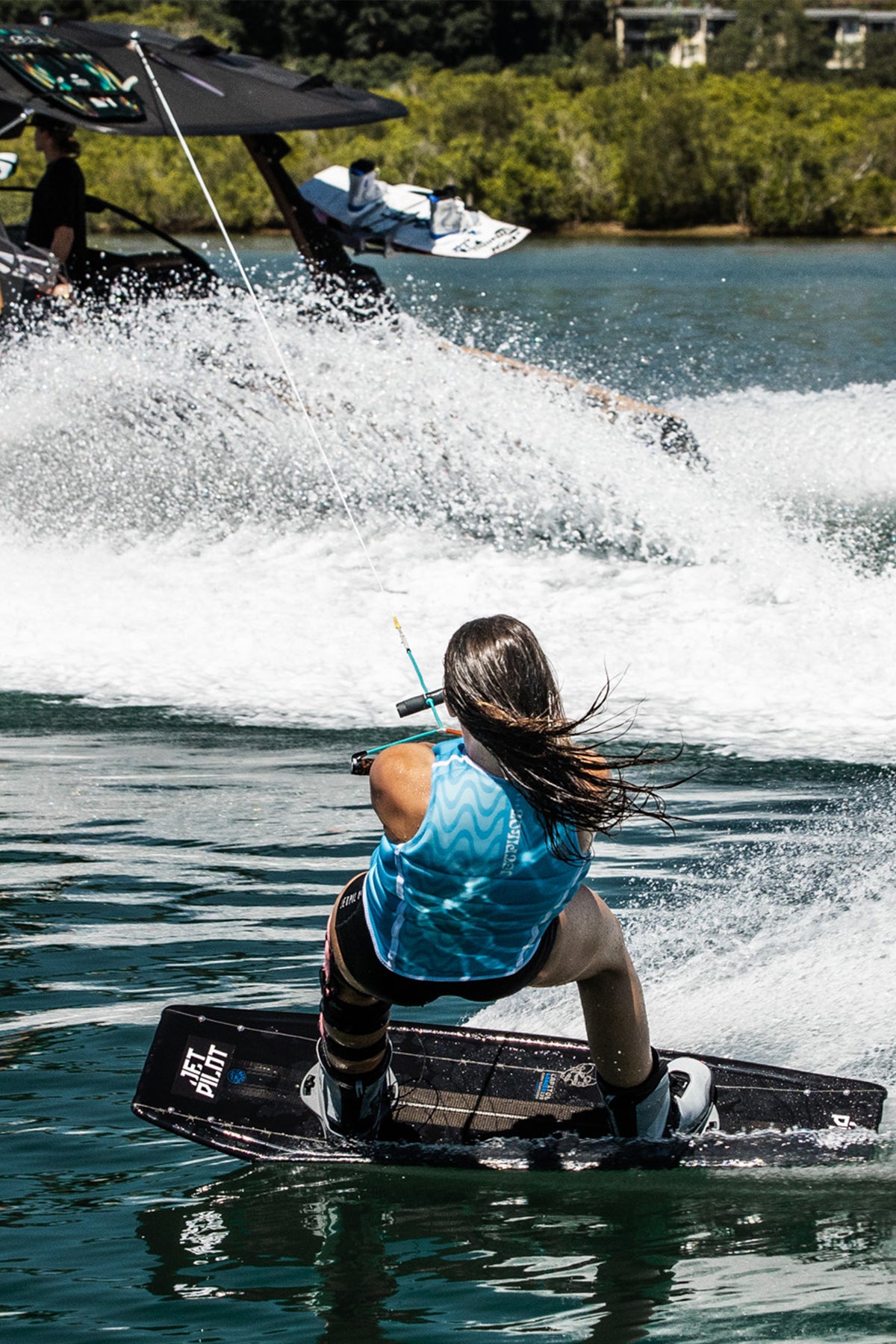 Rider carving on a wakeboard behind the boat in the Blue Luna life jacket, seen from behind