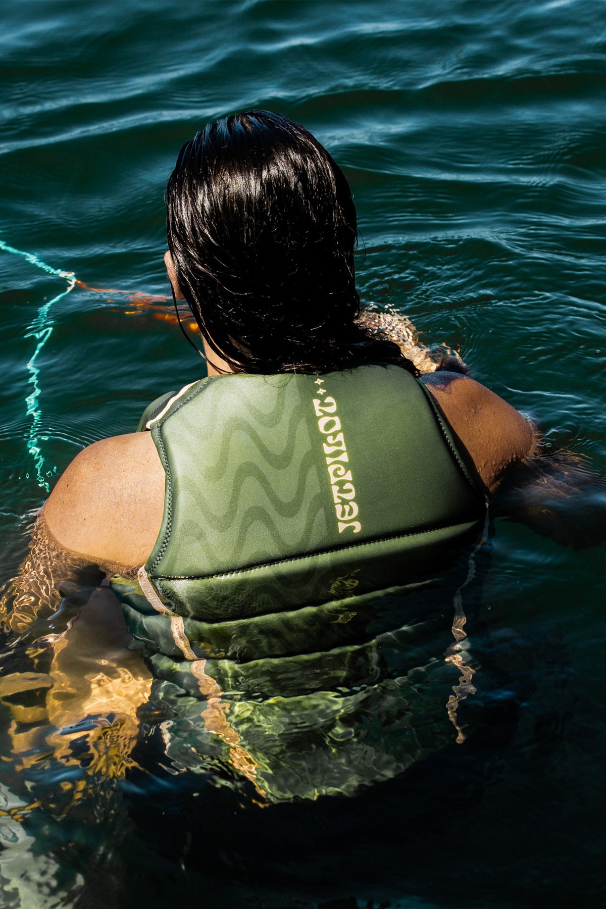 Rider floating in the water holding the tow rope, wearing the Olive Luna life jacket, seen from behind