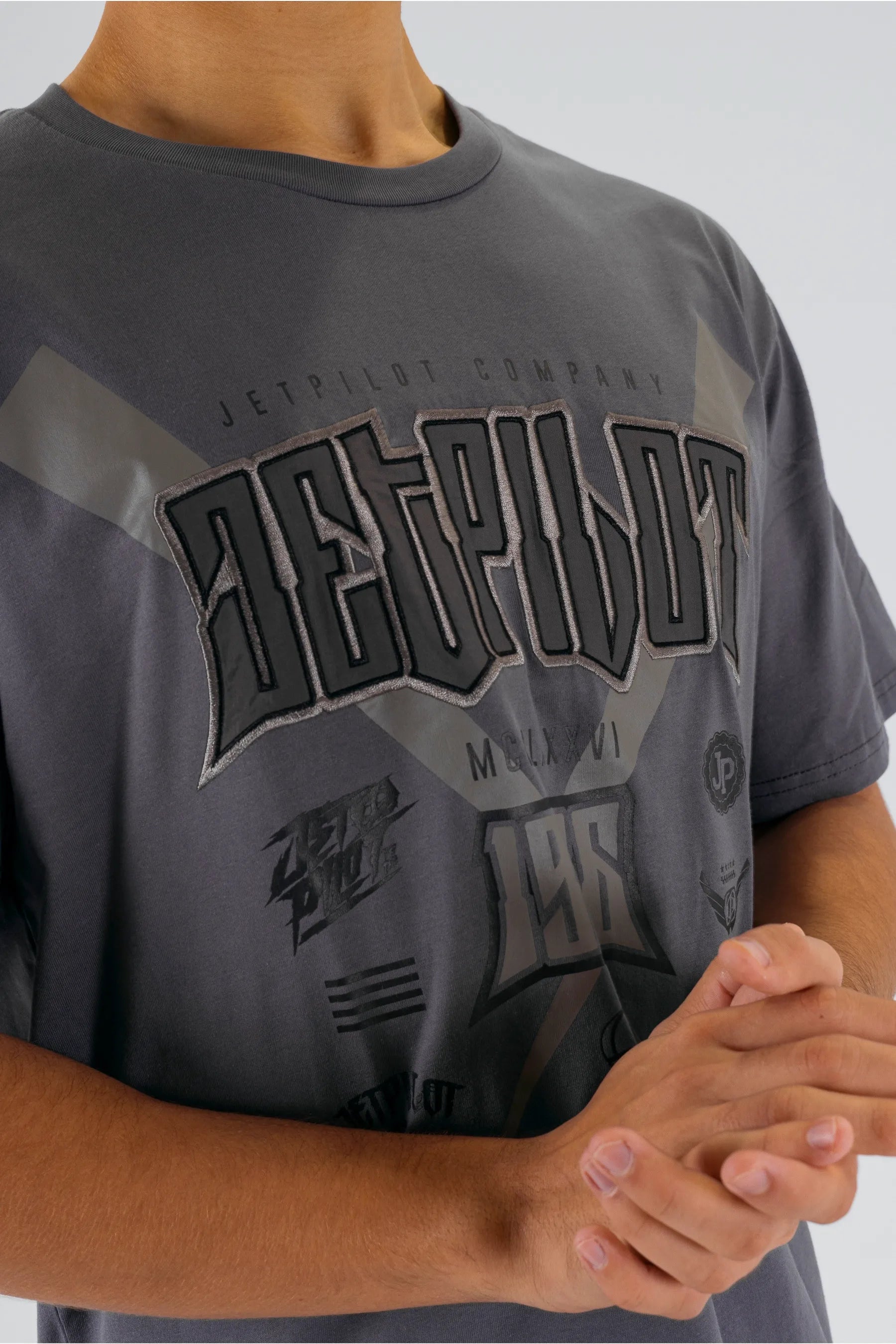 Close up of a person wearing a charcoal tee with a Jetpilot logo on a white background — view 3 (3)