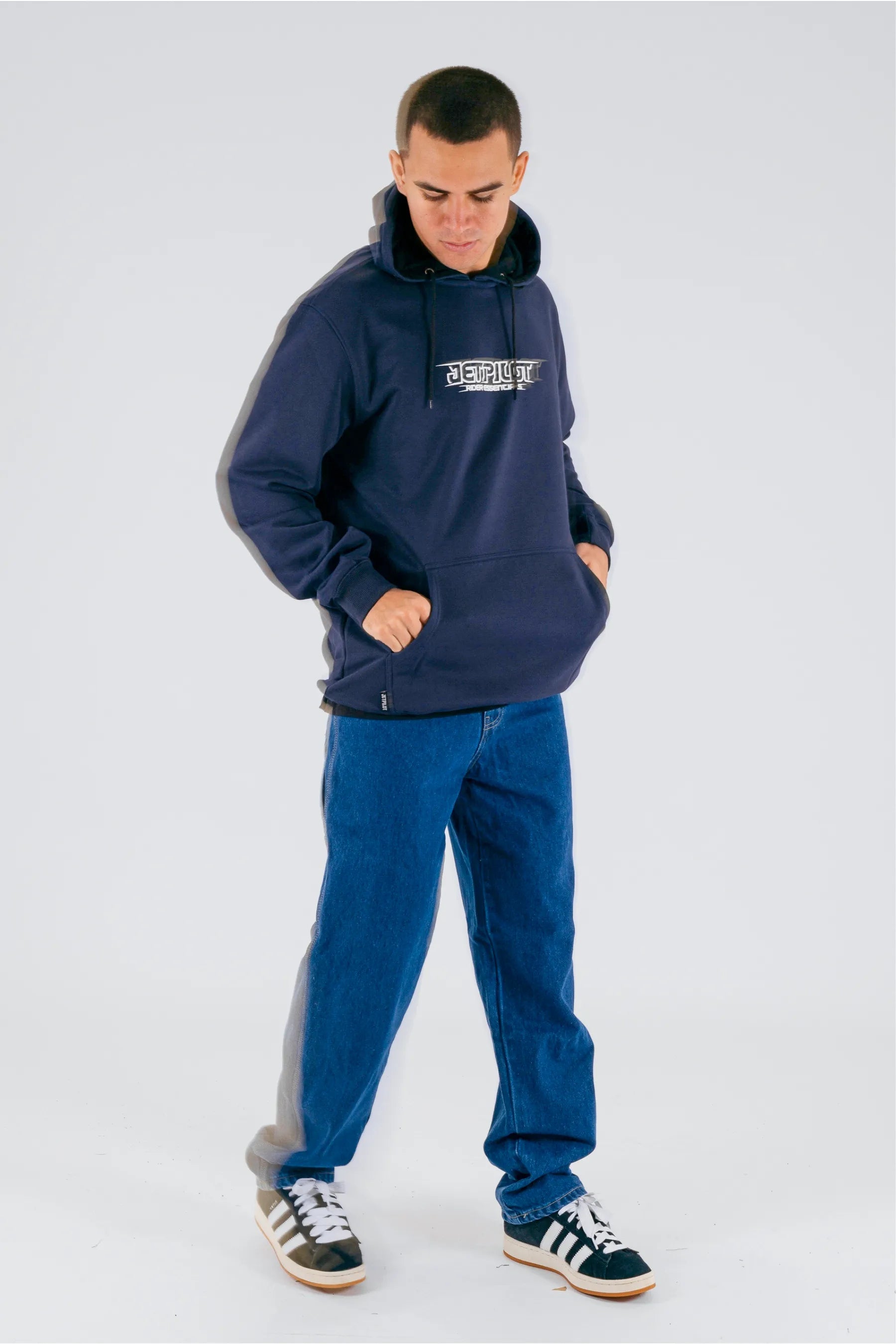 a person wearing a dark blue pullover with a Jetpilot logo, blue jeans and a black/white shoes — view 3 (3)