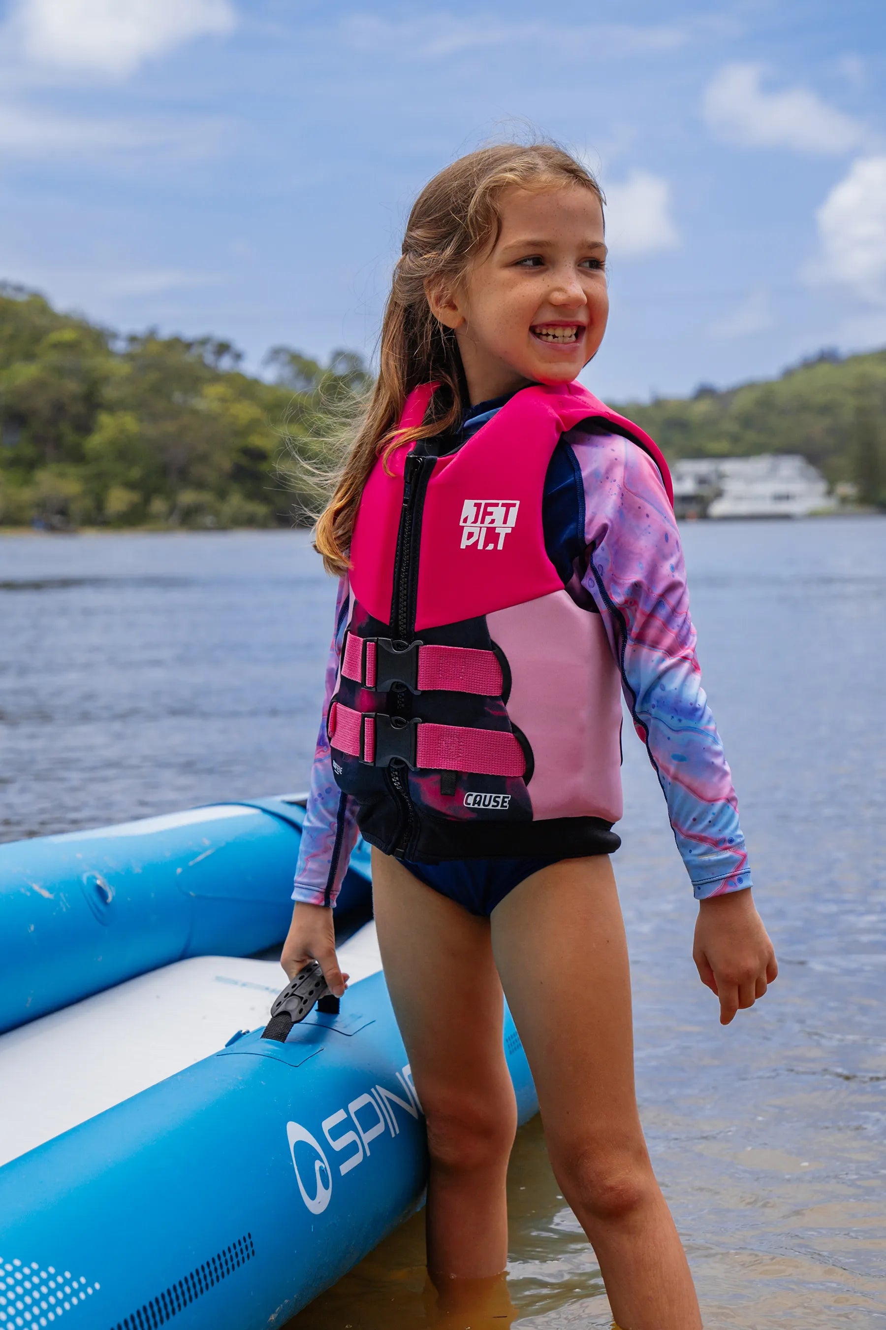 Young girl in a Cause Kids Life Jacket - Pink standing next to an inflatable boat on a lake.