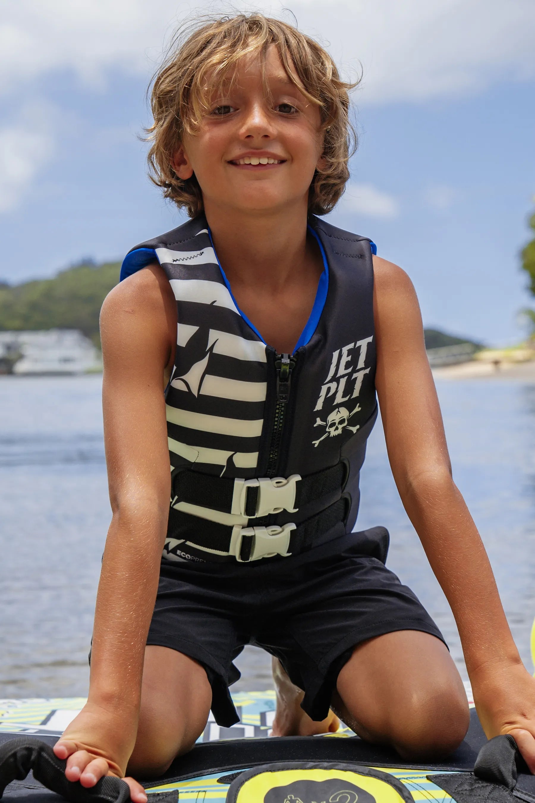 Child wearing a life jacket on a watercraft with a lake and sky background
