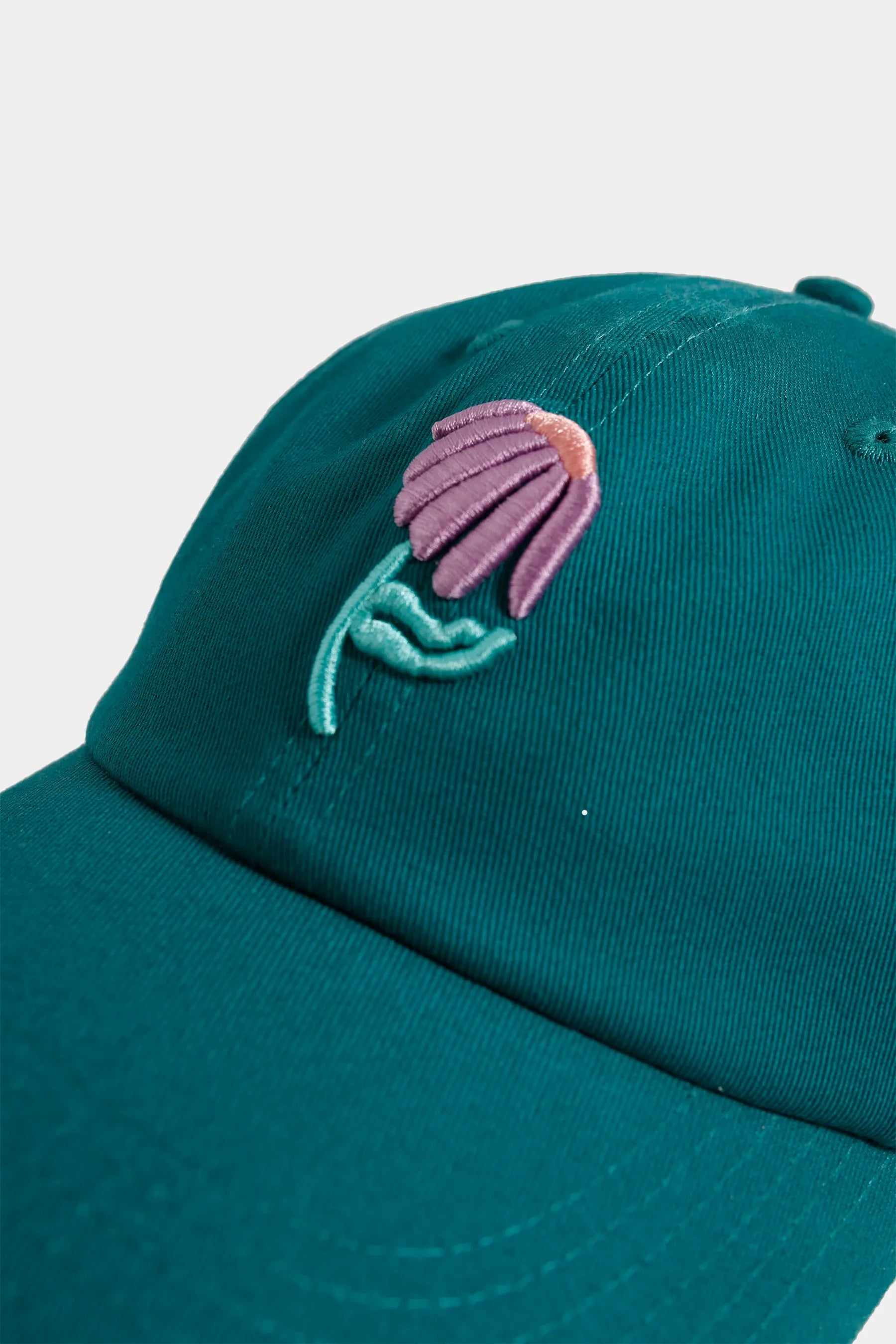 Teal cap with a pink and green embroidered flower design on a light grey background